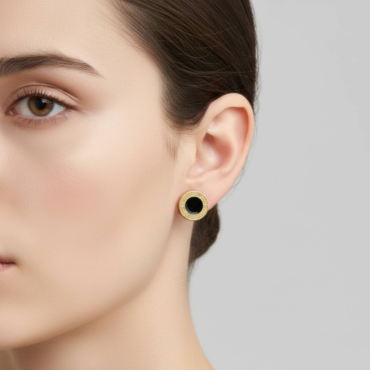 Close-up of a woman wearing gold earrings with a black center on a neutral background