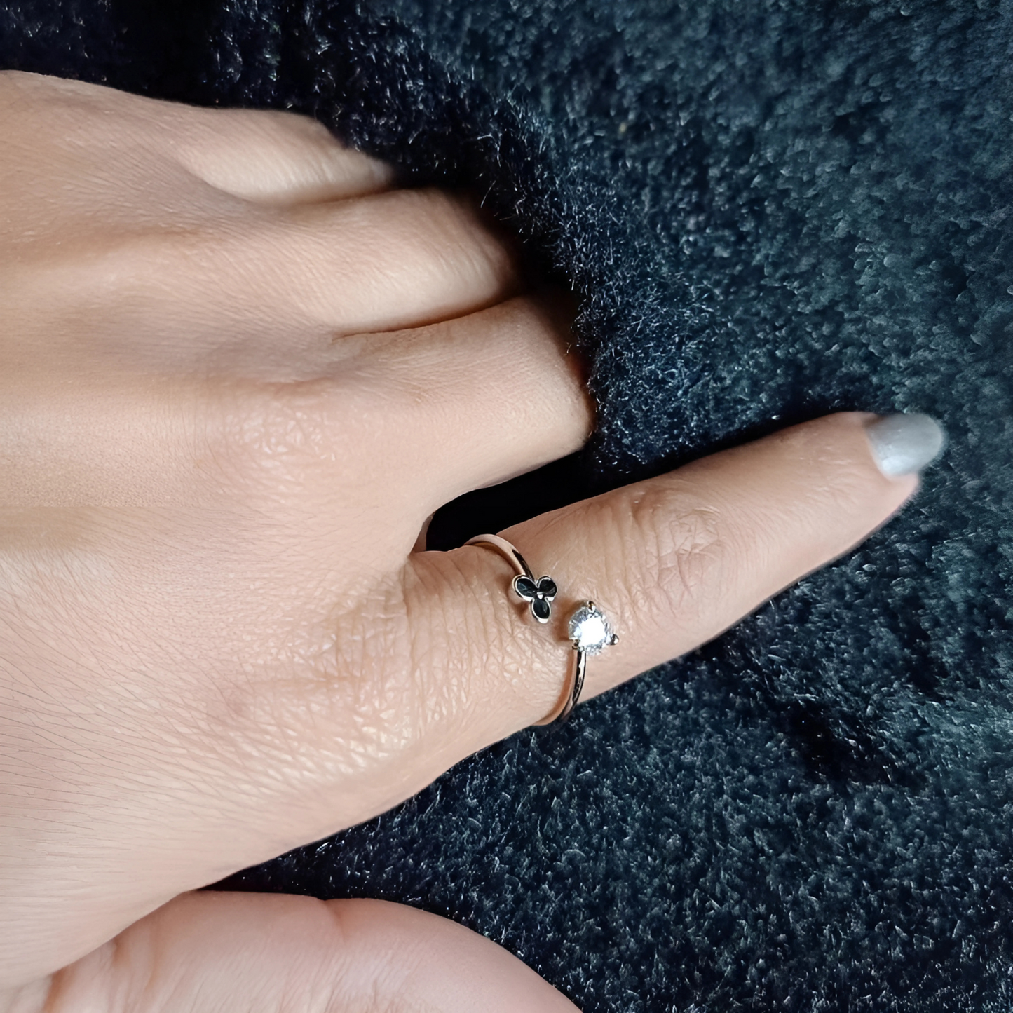 Hand wearing a delicate ring with a small diamond on a dark textured fabric background