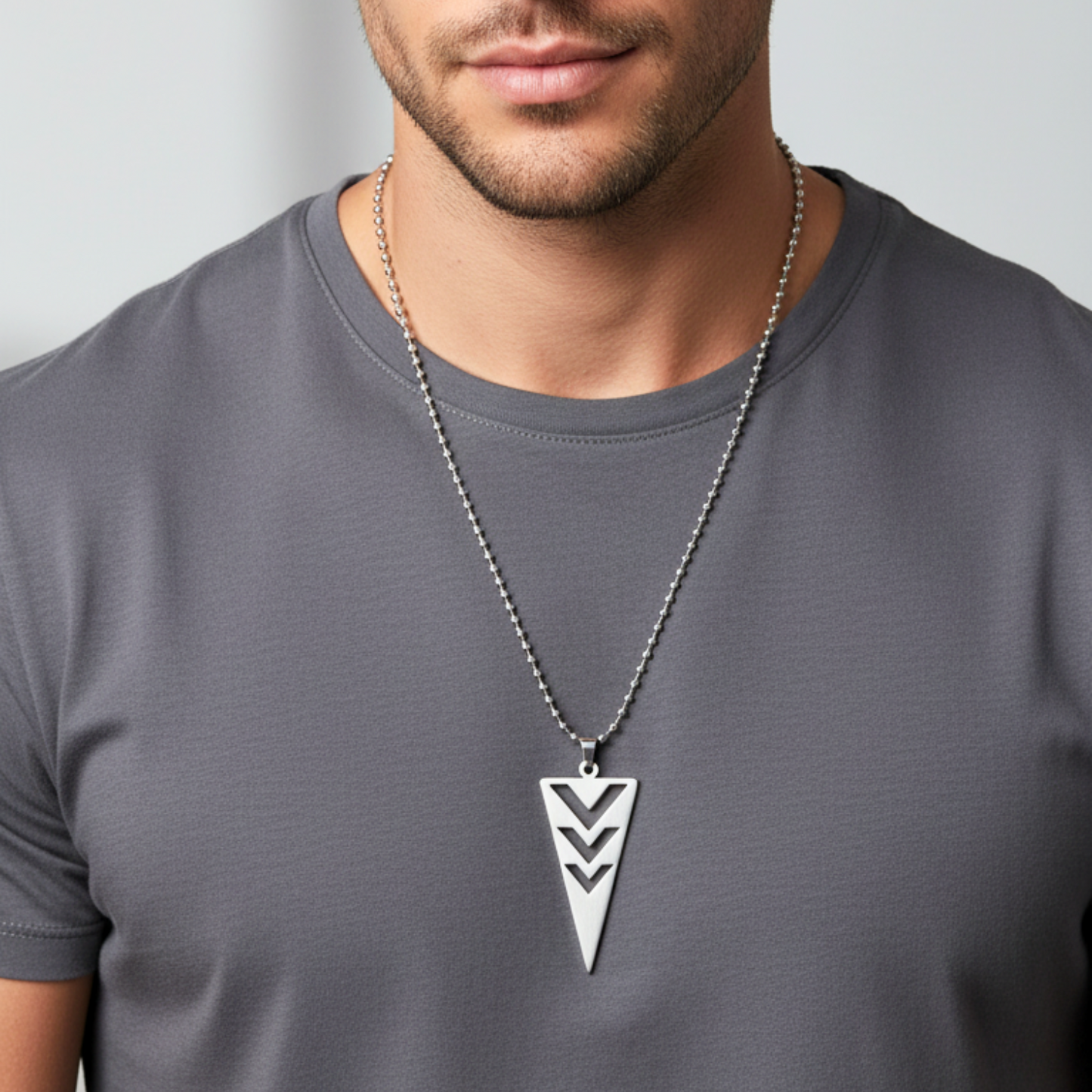Man wearing a gray t-shirt with a necklace featuring a triangular pendant.