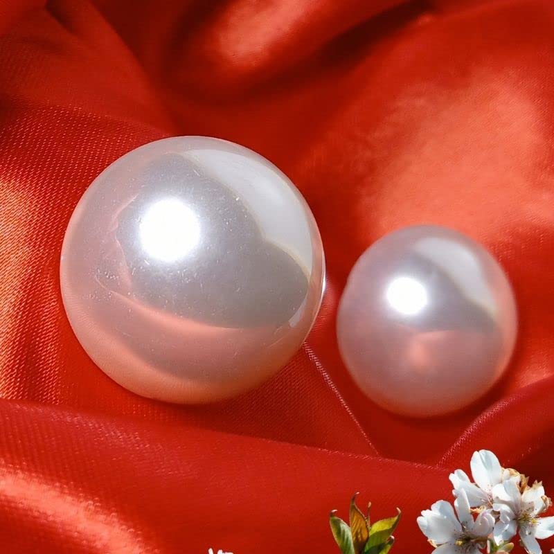 Two pearls on a red fabric background with a small plant and flowers at the bottom.