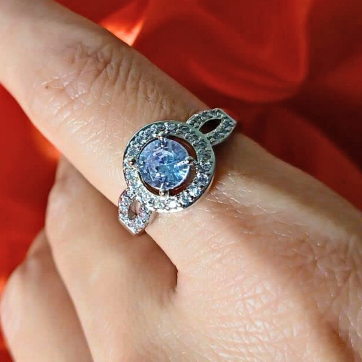 Silver ring with a blue gemstone on a finger against a red background