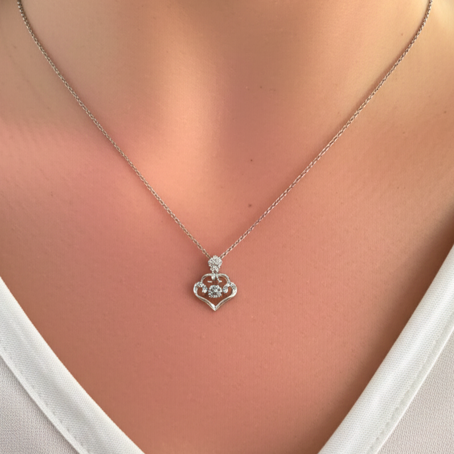 Silver necklace with a claddagh pendant on a person wearing a white top.