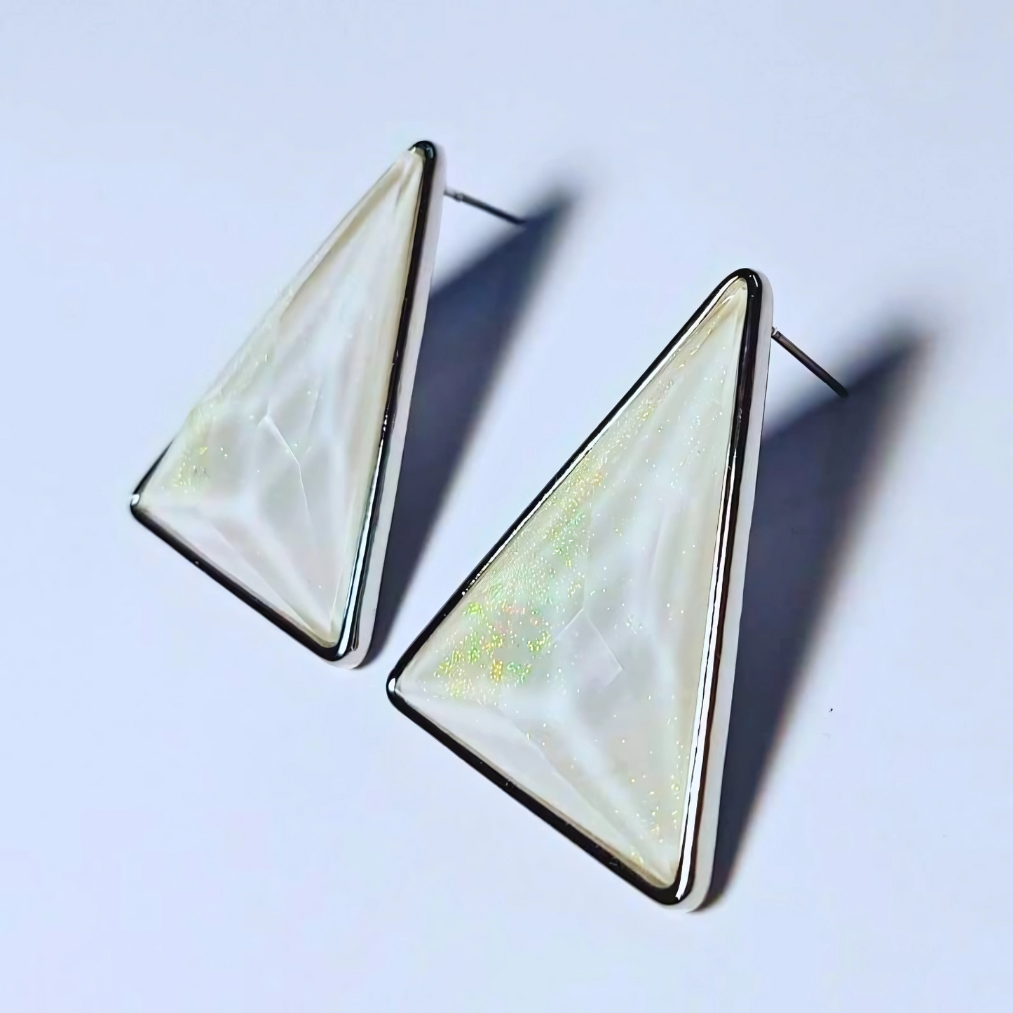 Triangular earrings with a white and gold design on a light blue background