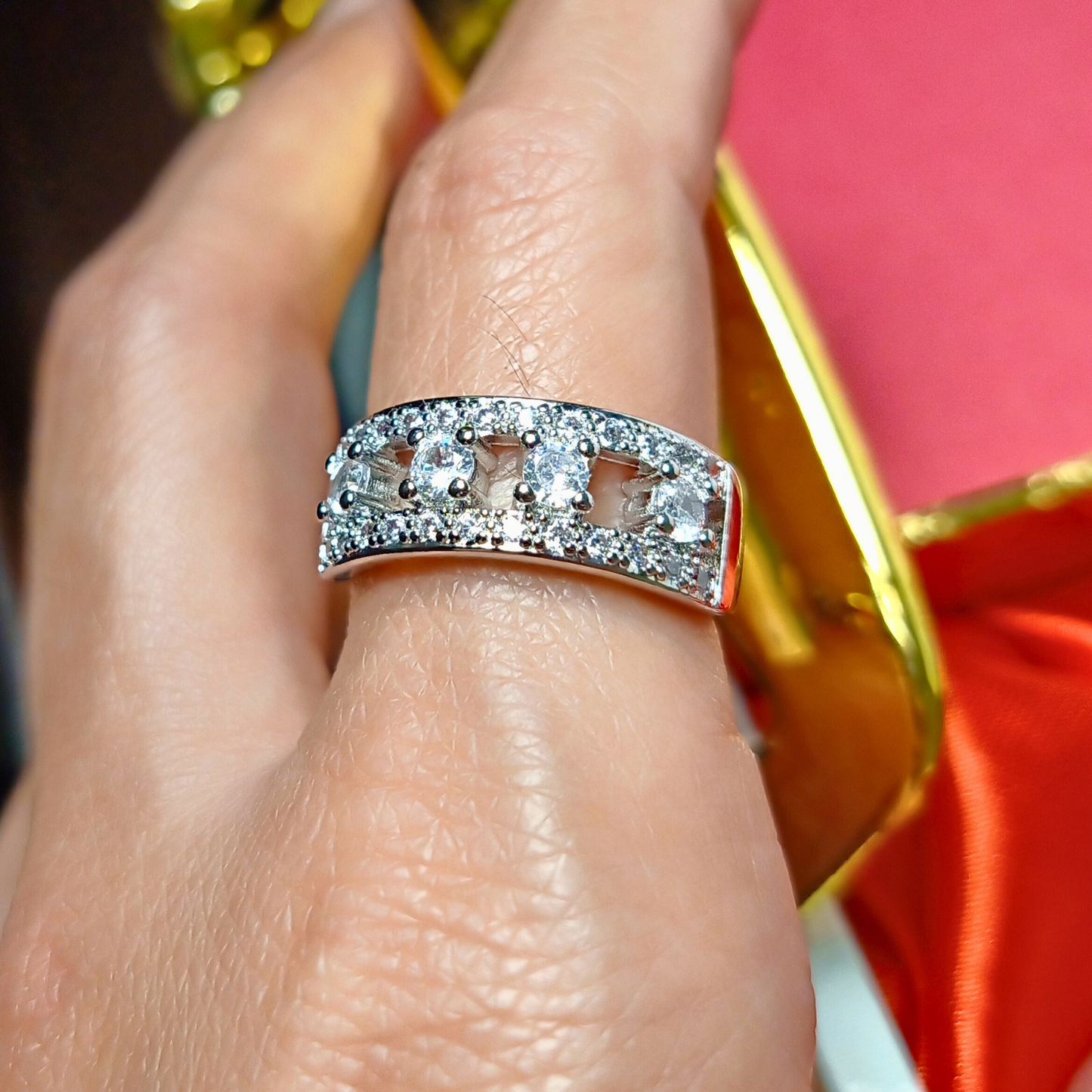 Silver ring with diamonds on a finger against a red and gold background