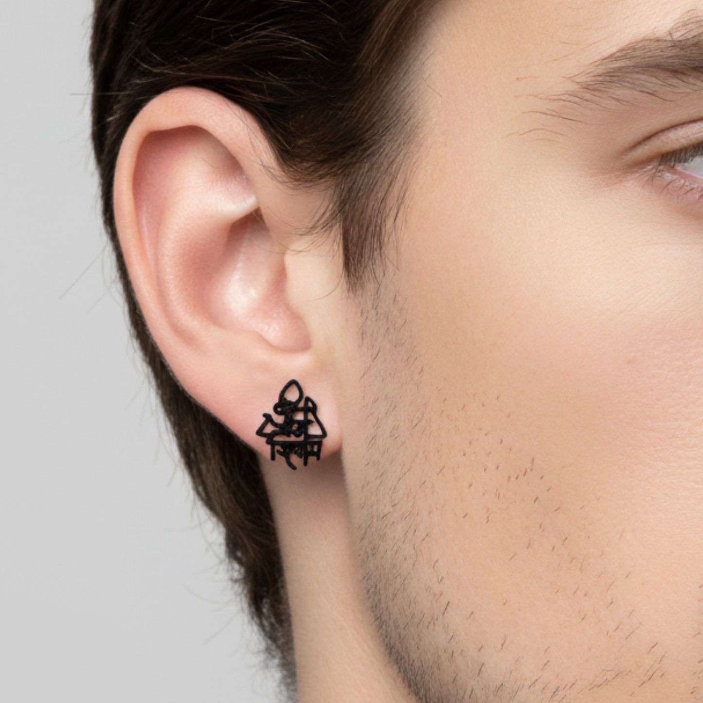 Black geometric earring on a person's ear against a neutral background