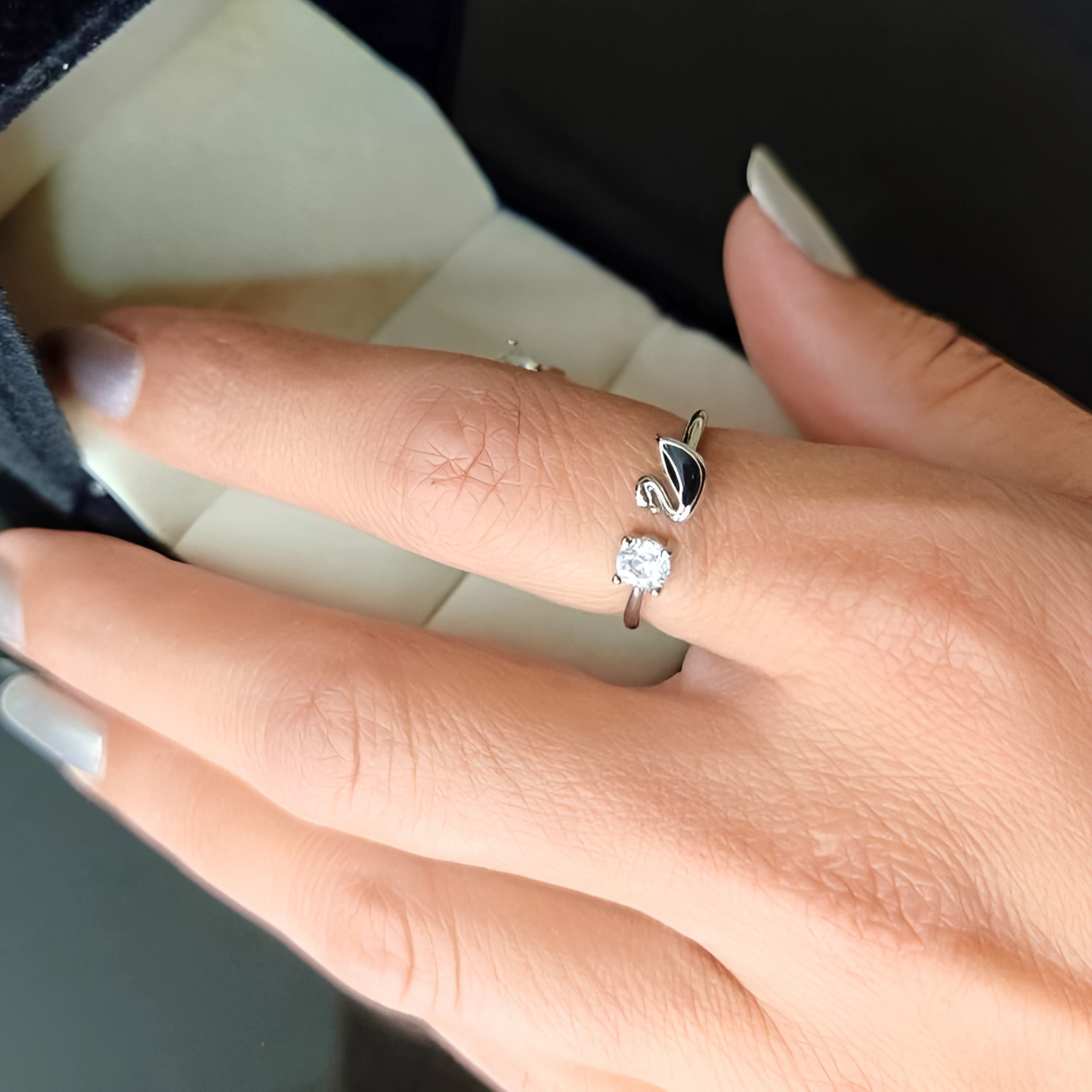 Hand wearing a silver ring with a diamond on a neutral background