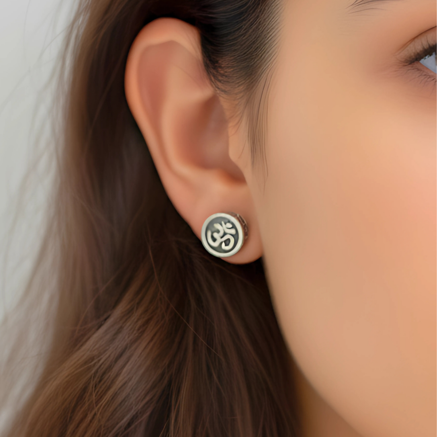 Close-up of an ear wearing a silver Om symbol earring with blurred background