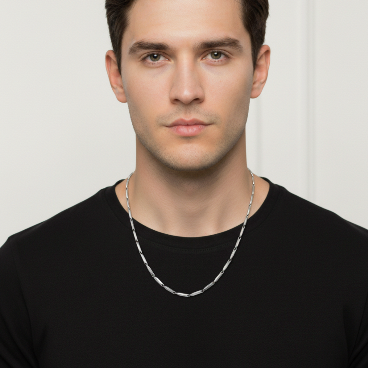 Man wearing a silver chain necklace against a plain background