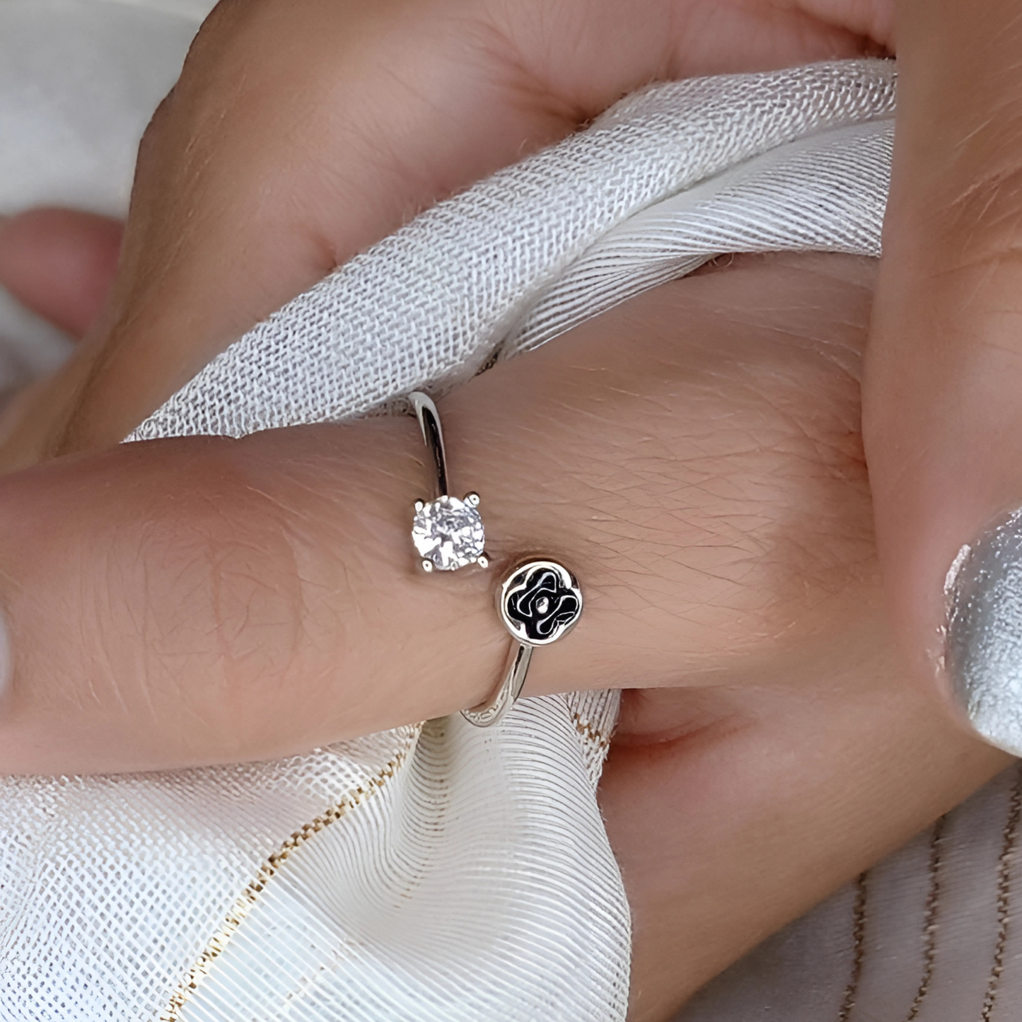 Close-up of a hand wearing two silver rings with a diamond on a white fabric background