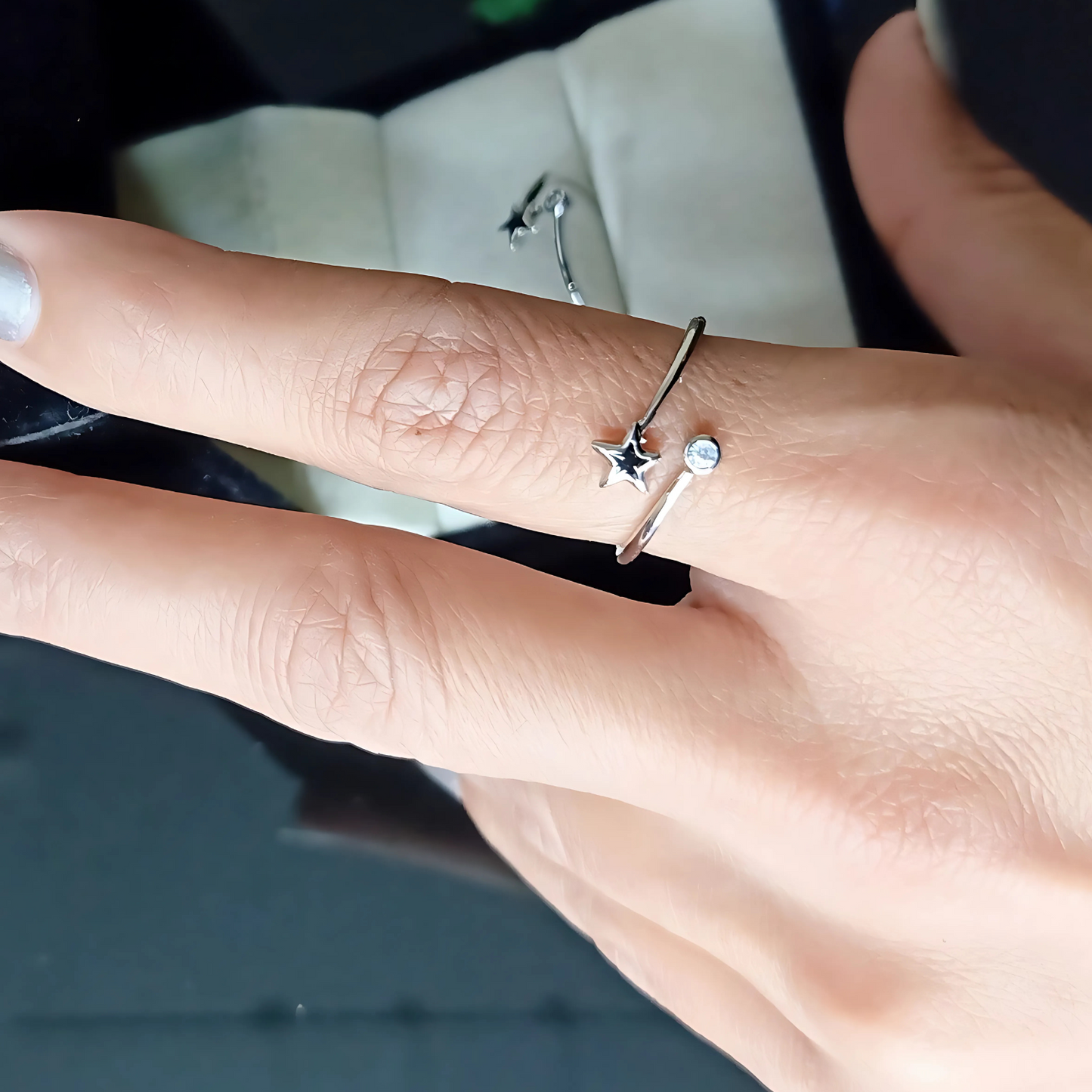 Silver ring with star design on a person's finger against a blurred background
