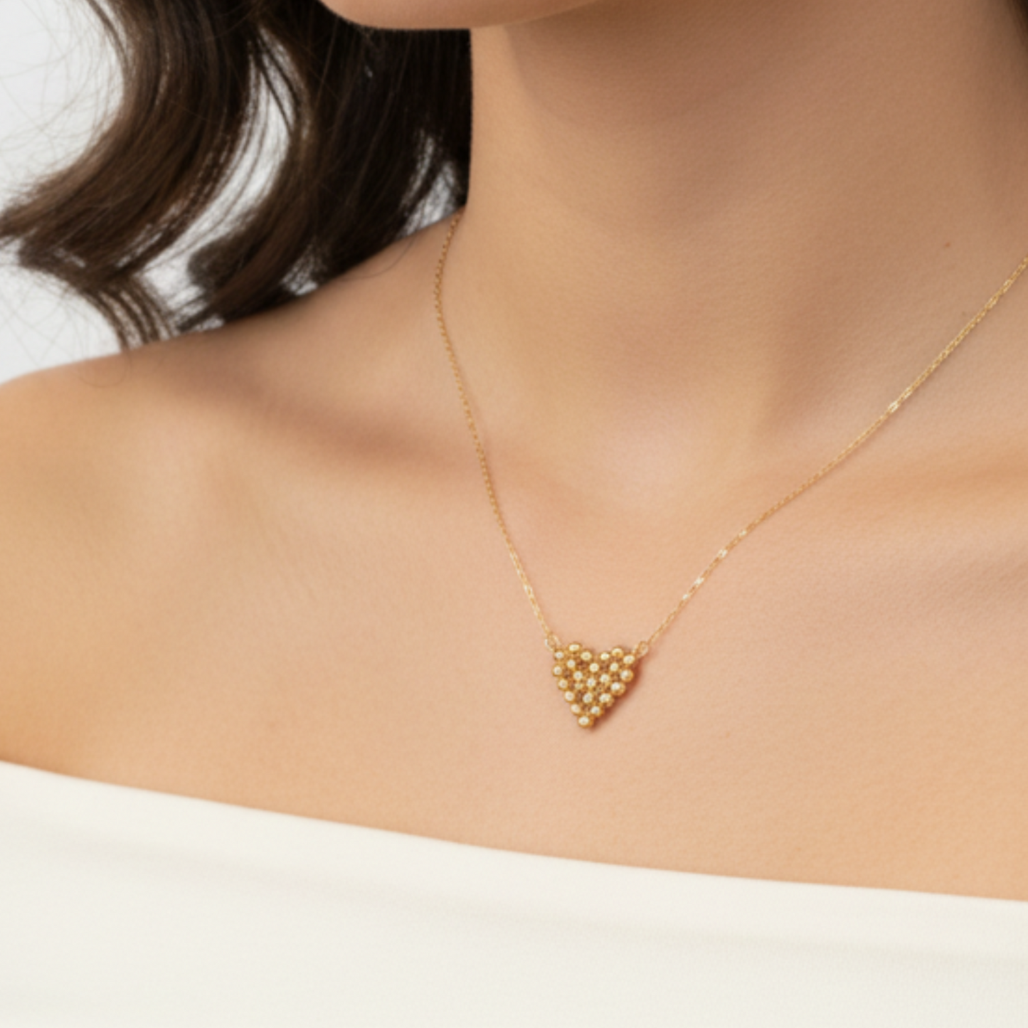 Gold necklace with a heart-shaped pendant on a person wearing a white top.