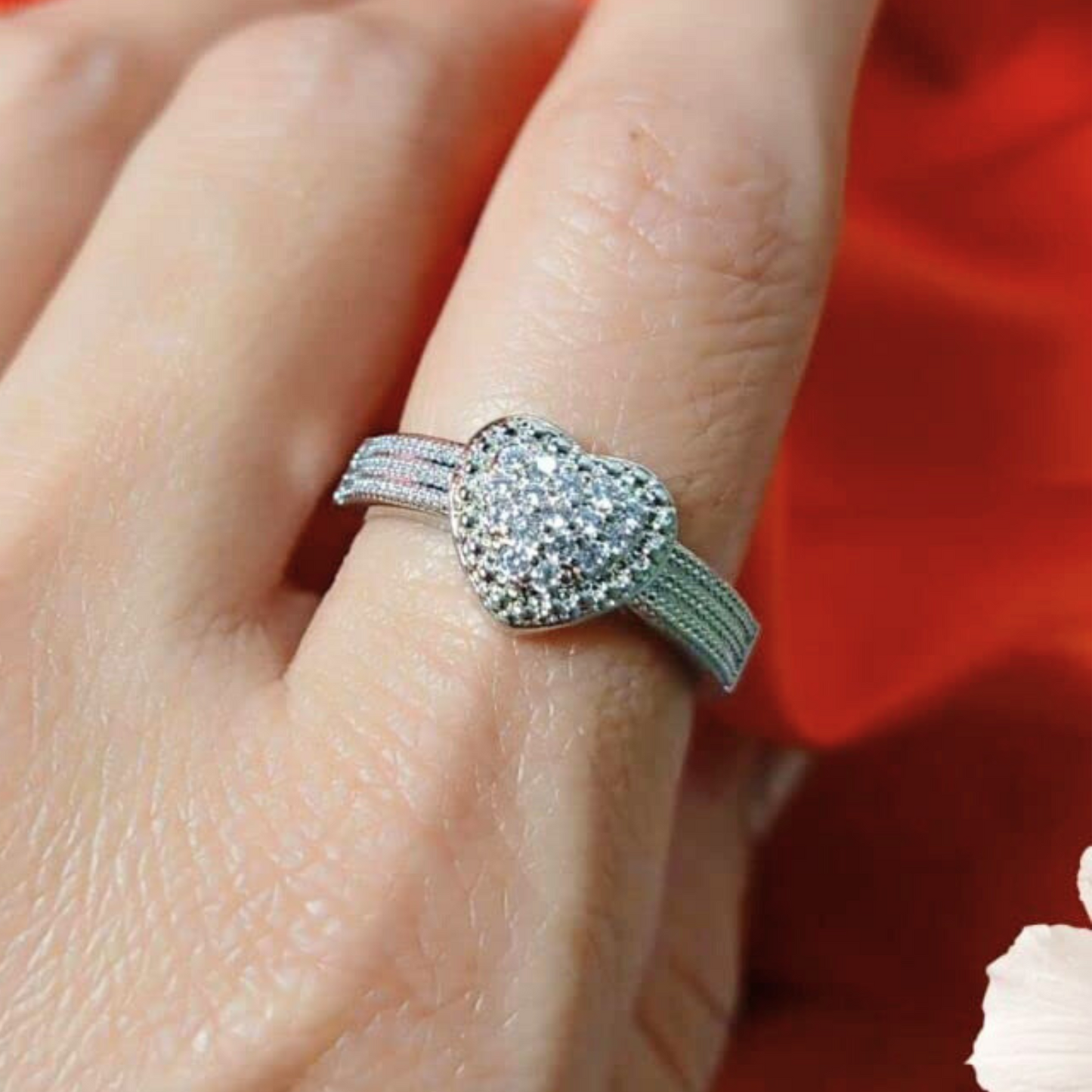 Silver ring with gemstones on a finger against a red background