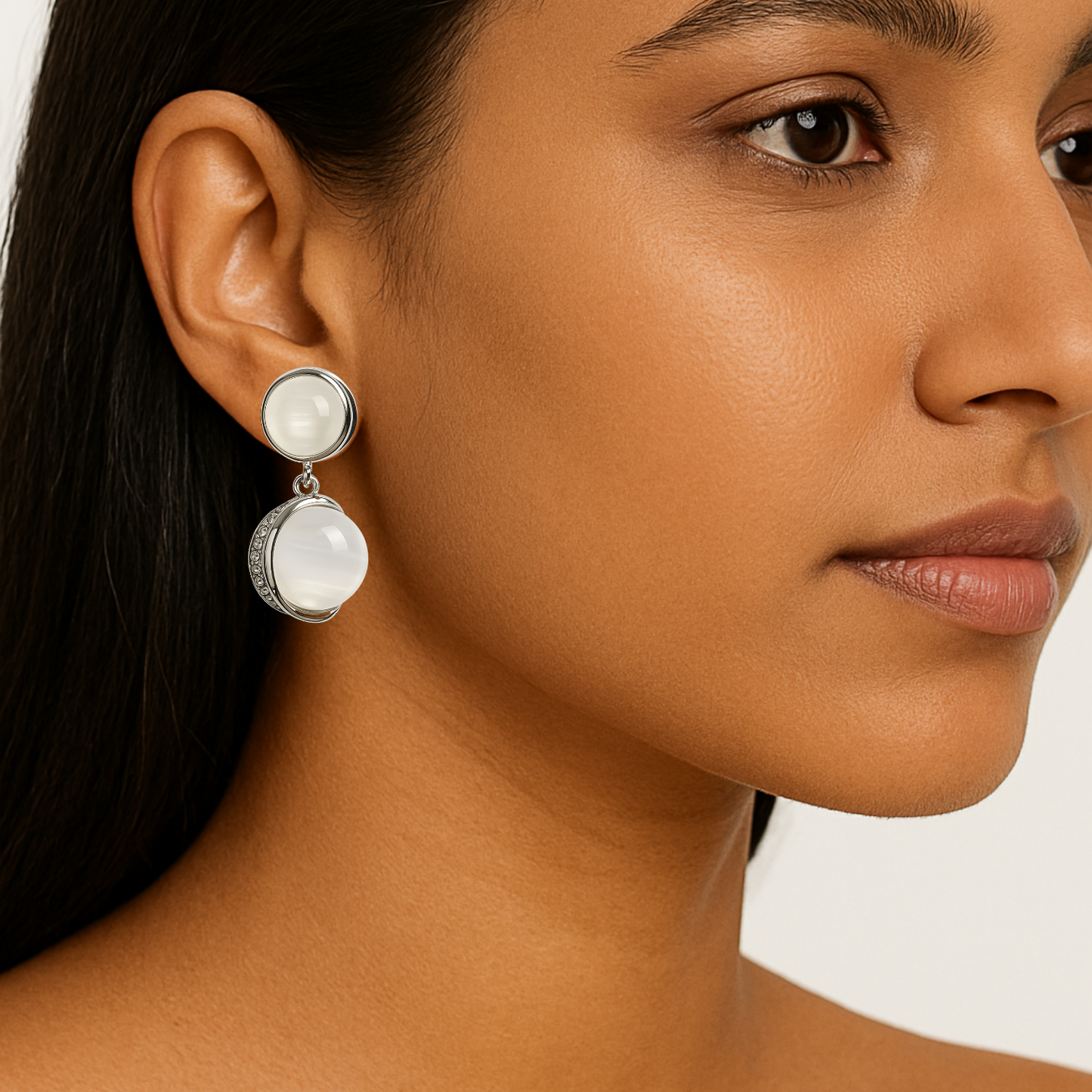 Close-up of a woman wearing a silver earring with a white stone on a neutral background