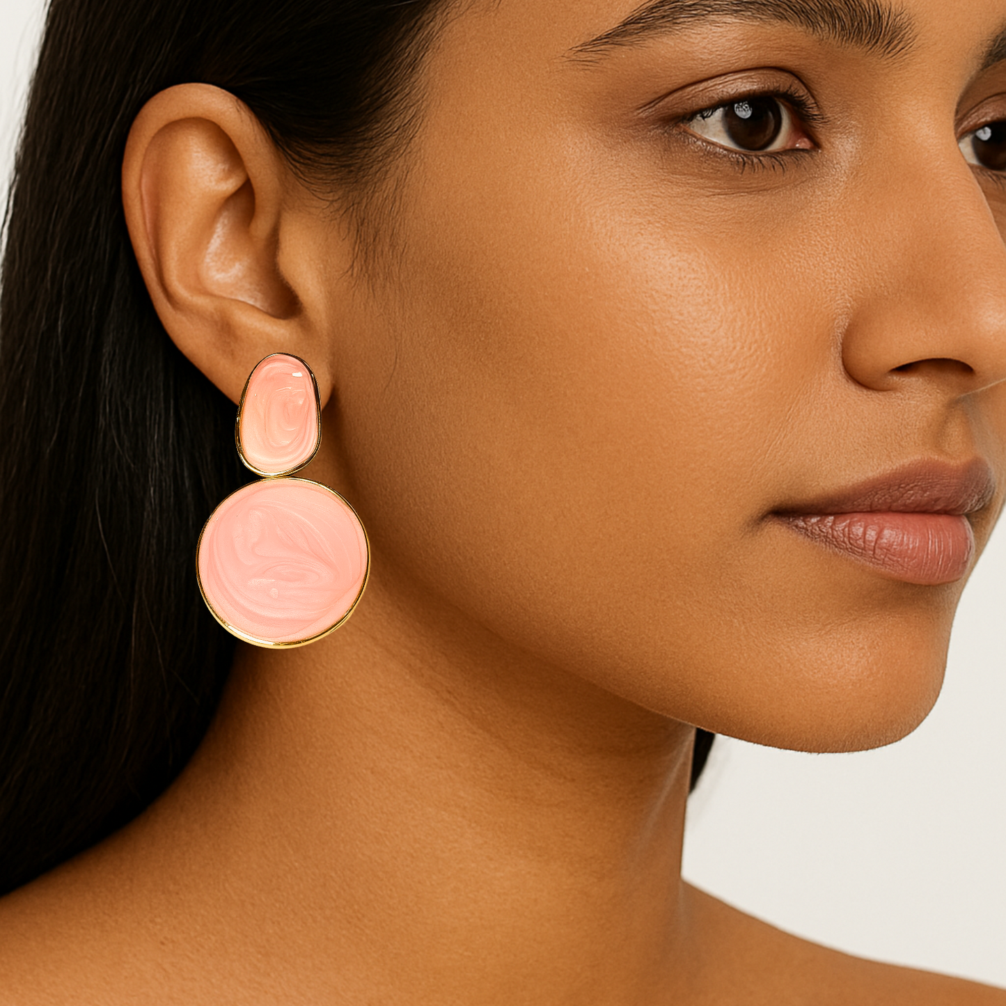 Close-up of a woman wearing pink circular earrings with gold accents.