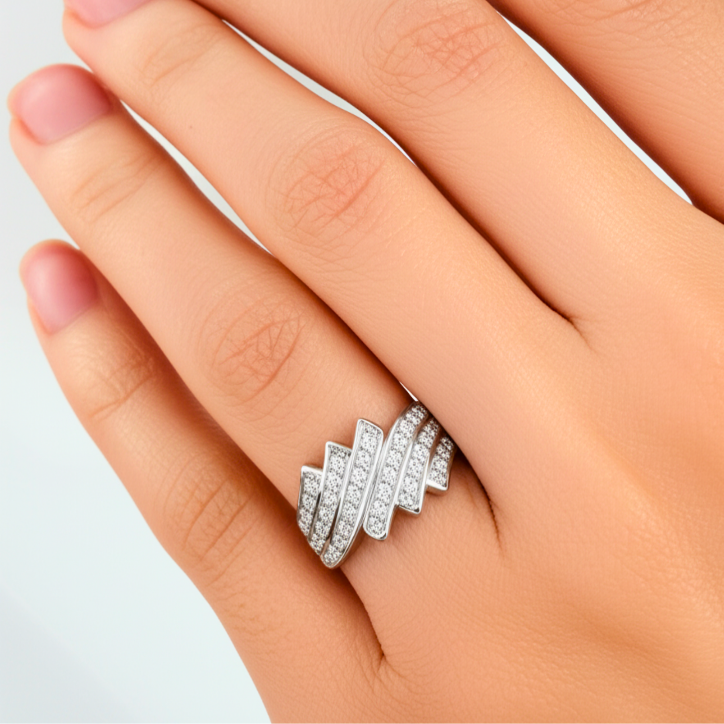 Silver ring with diamonds on a hand against a light gray background