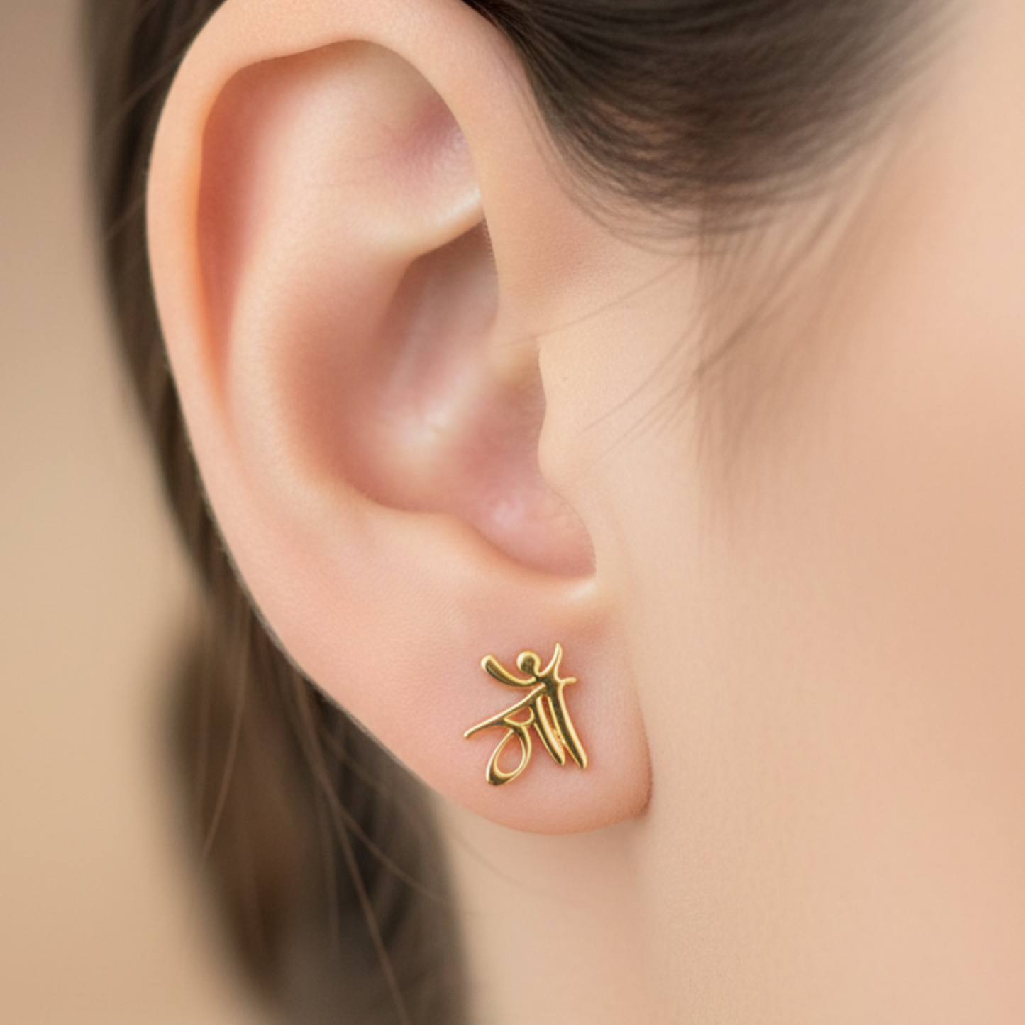 Gold earring worn on an ear with a blurred background