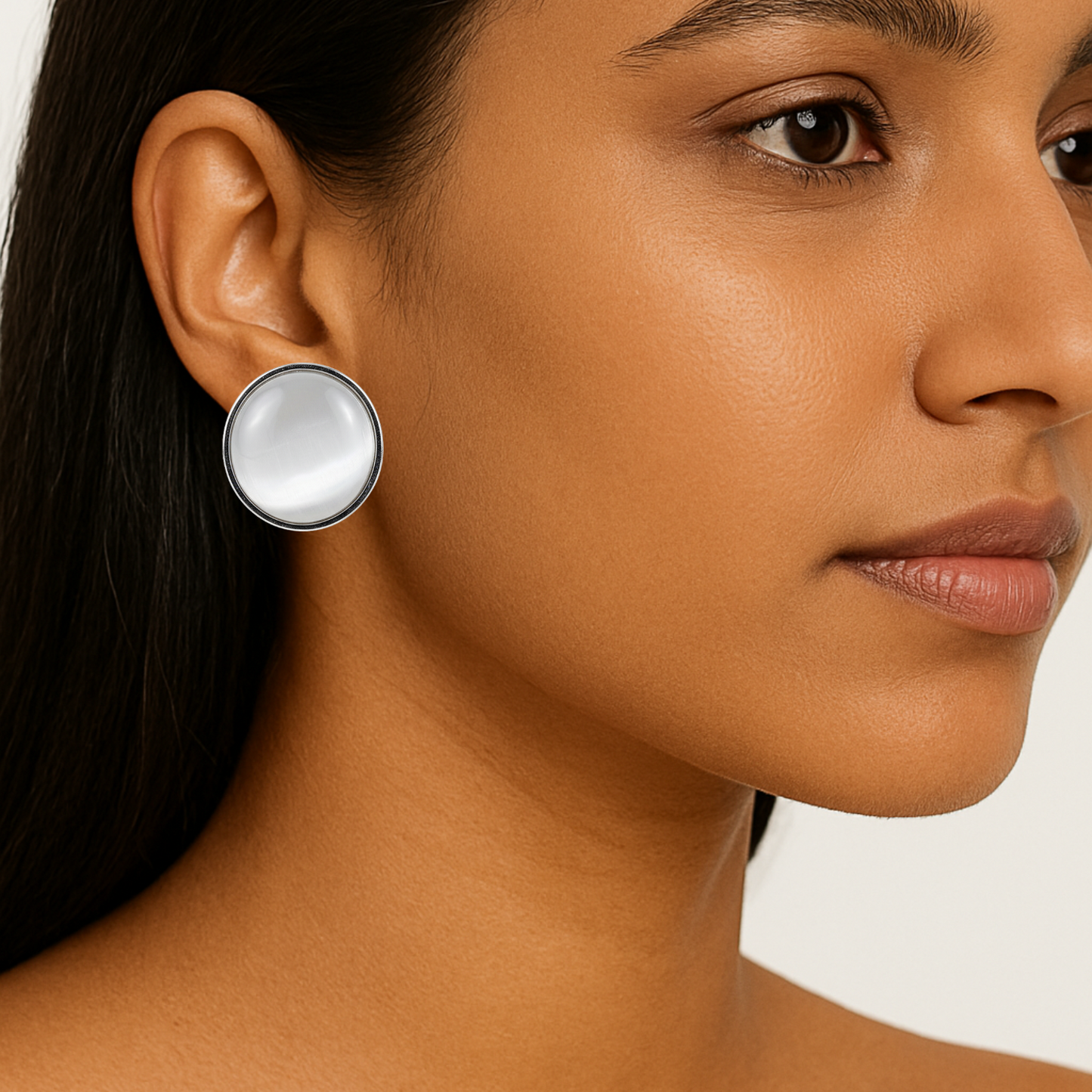 Close-up of a woman wearing a round earring with a white stone.