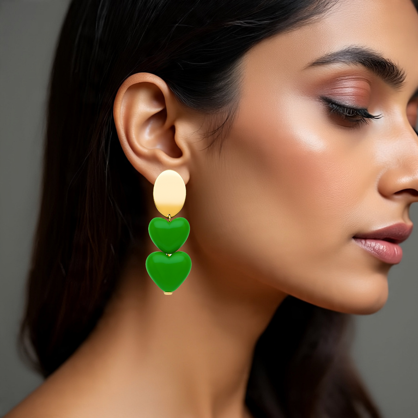 Close-up of a woman wearing green heart-shaped earrings against a neutral background