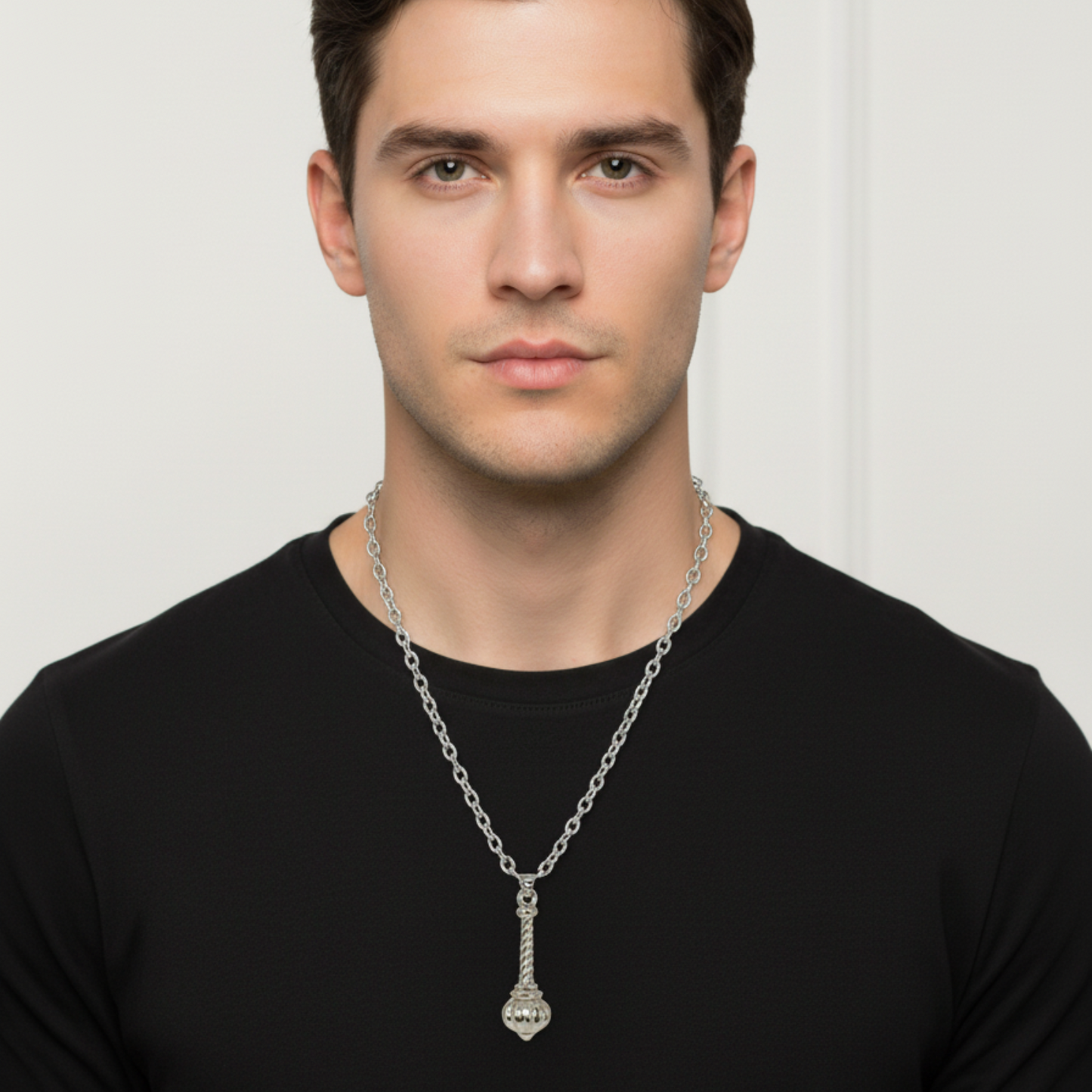 Man wearing a silver necklace with a pendant against a plain background