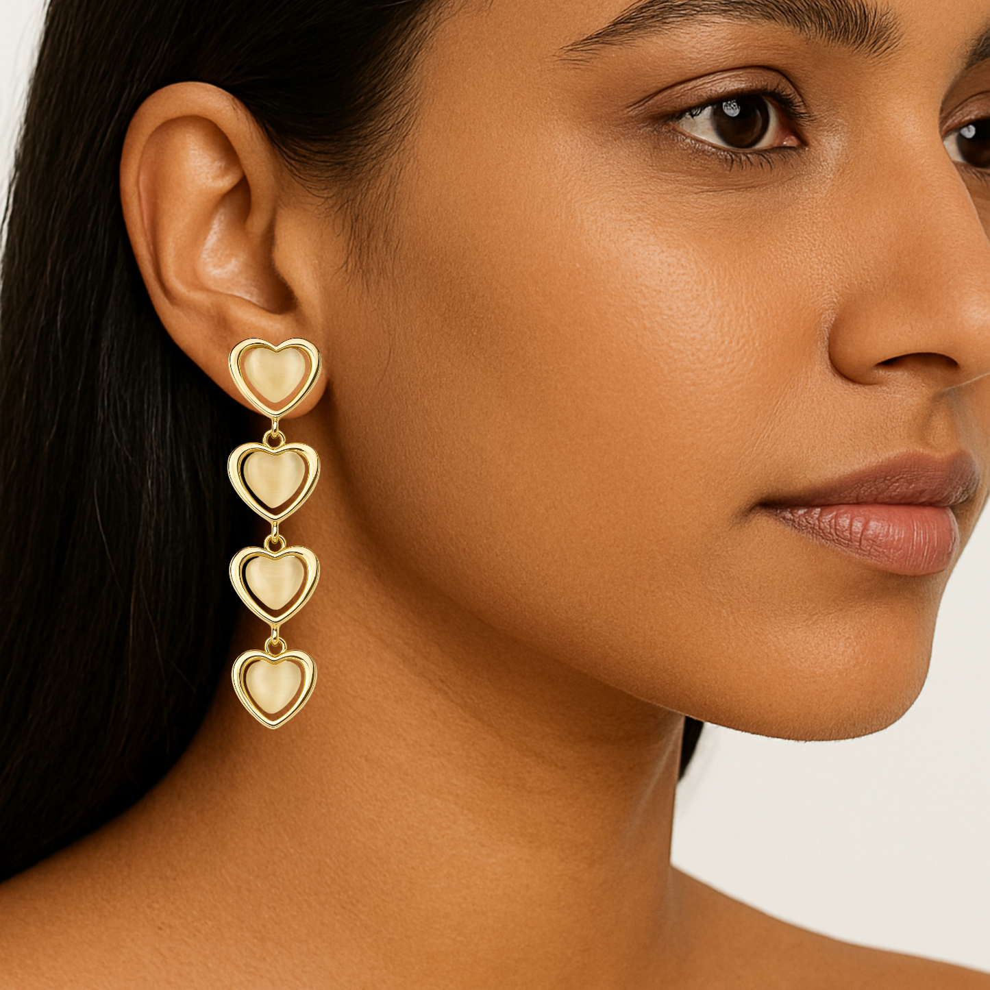 Close-up of a woman wearing gold heart-shaped earrings against a neutral background