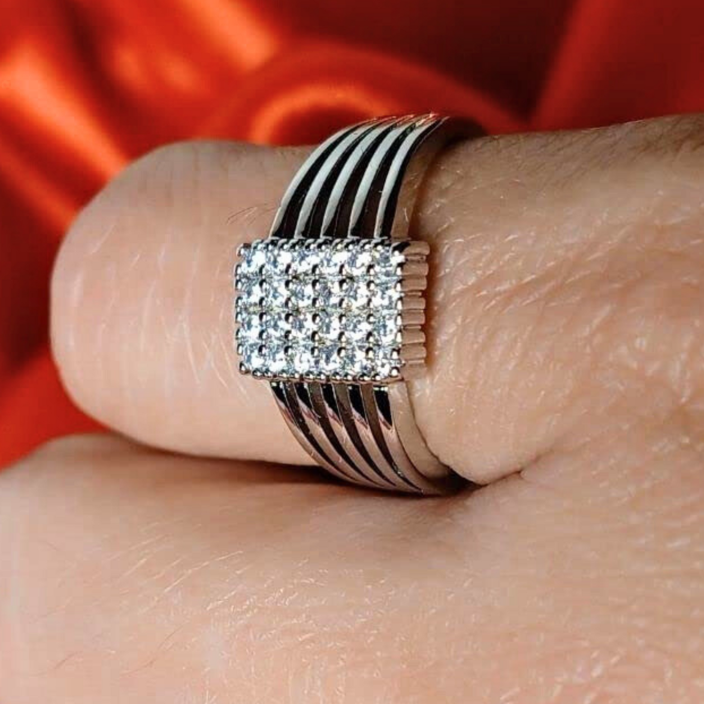 Silver ring with black and white striped band on a finger against an orange fabric background