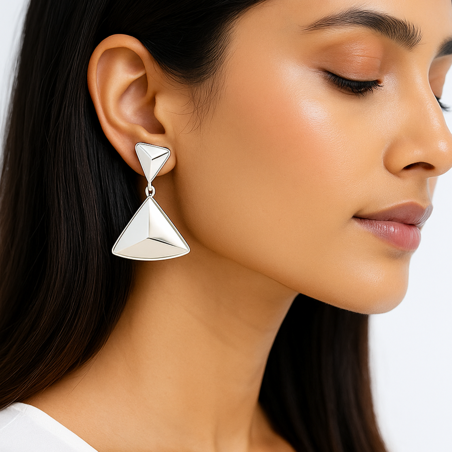 Close-up of a woman wearing silver triangle earrings with a plain background