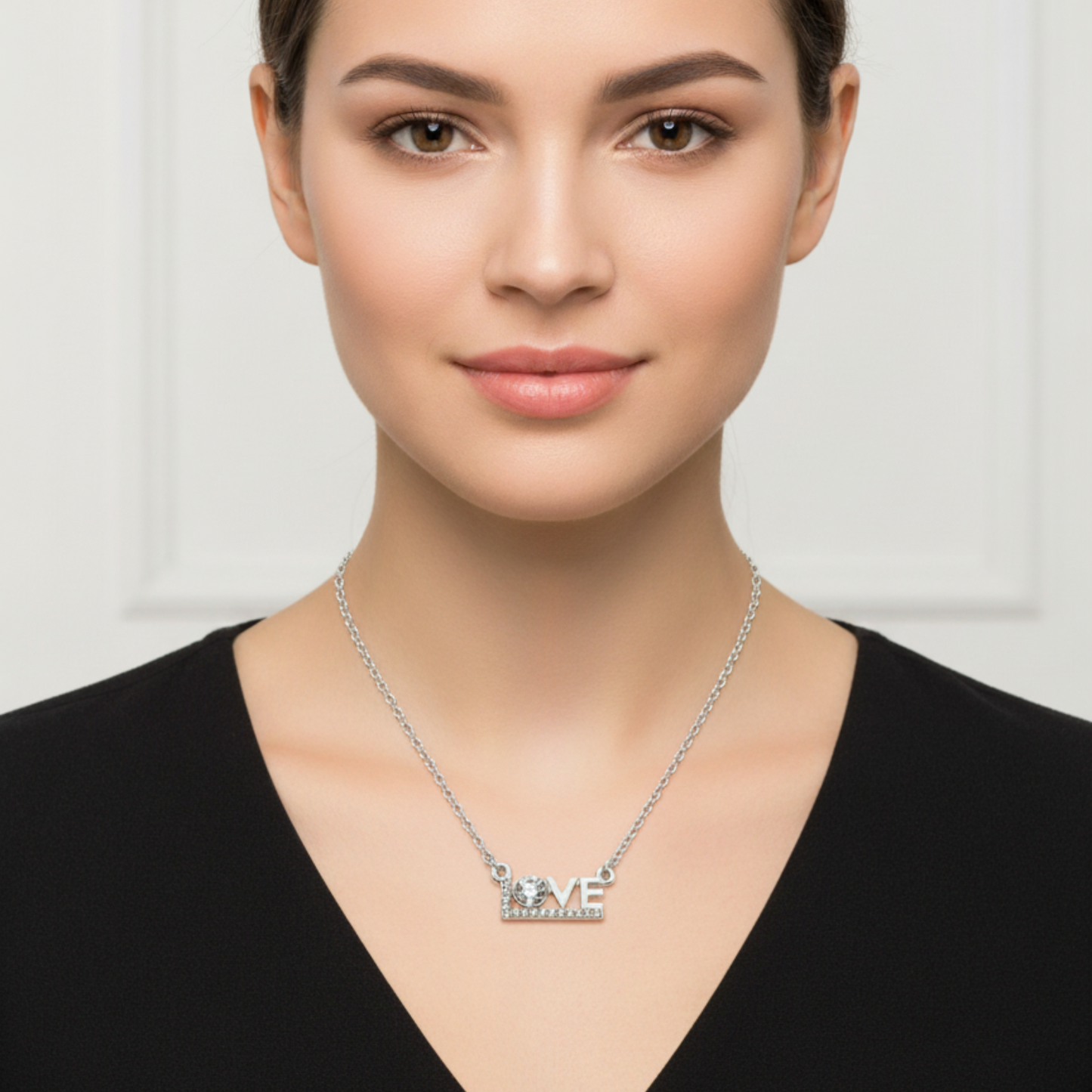 Woman wearing a silver necklace with 'LOVE' pendant on a plain background