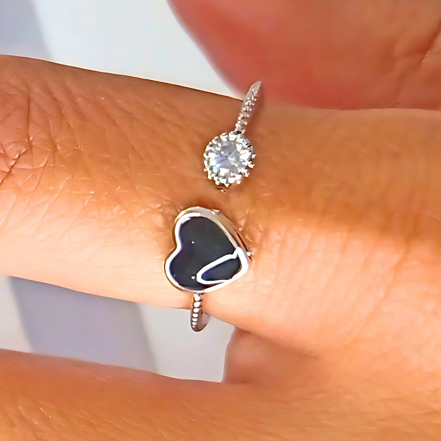 Close-up of a silver ring with a heart-shaped black stone on a finger.