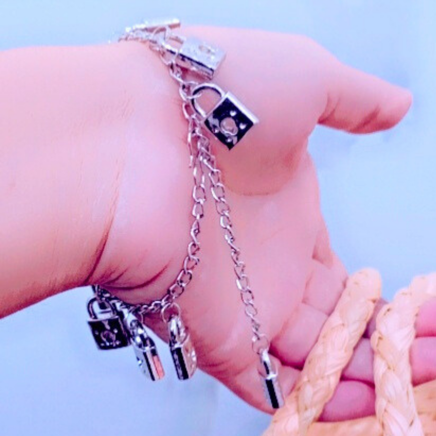 Hand wearing a silver bracelet with padlock charms against a light blue background