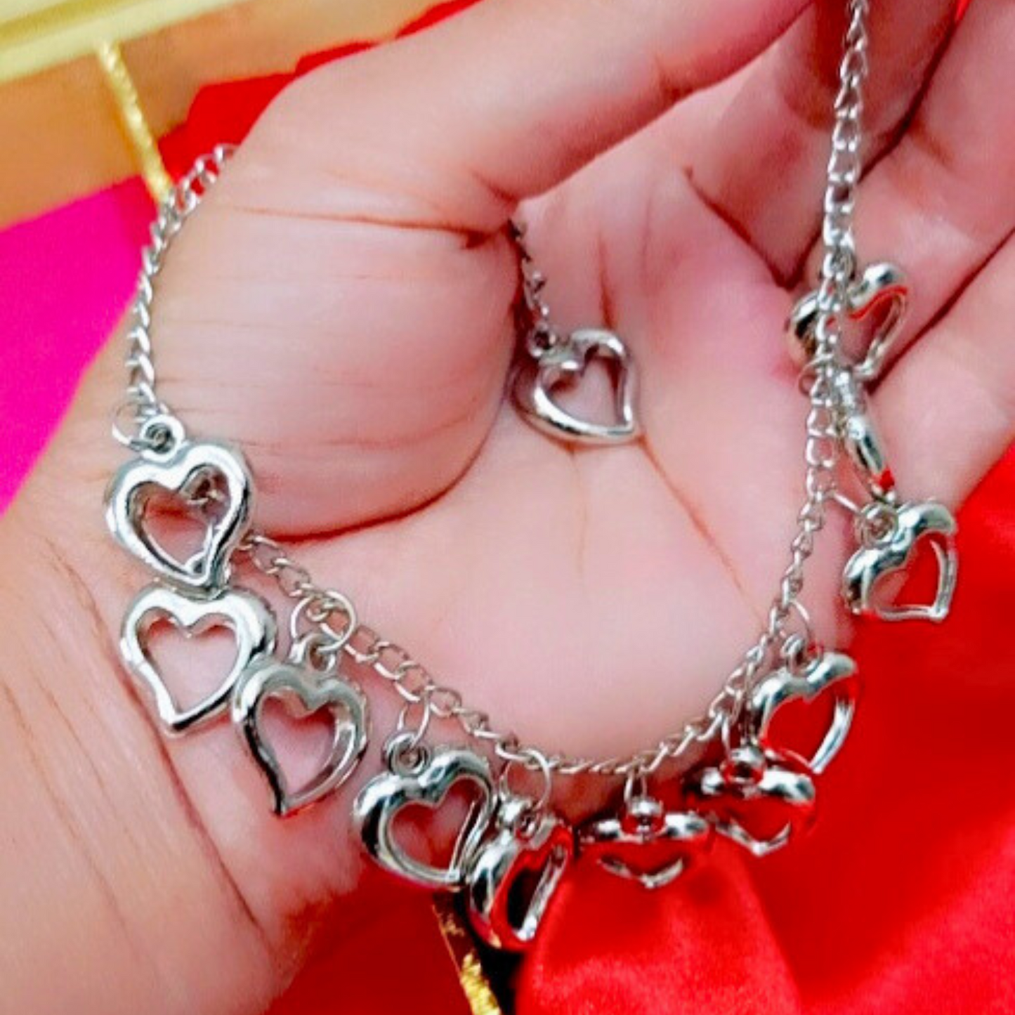 Silver heart-shaped bracelet on a hand with a red background