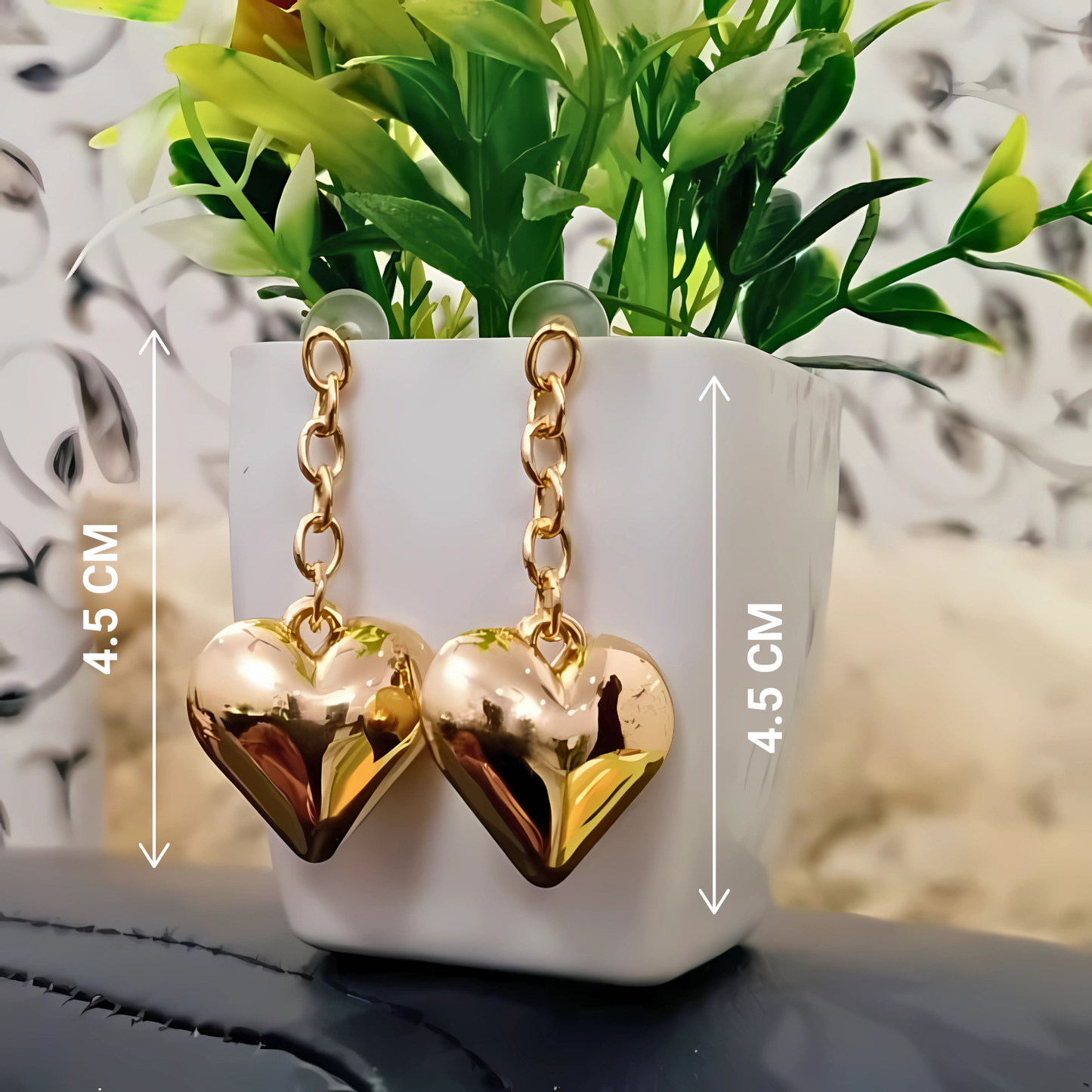 Gold heart-shaped earrings on a stand with plant and measurement details