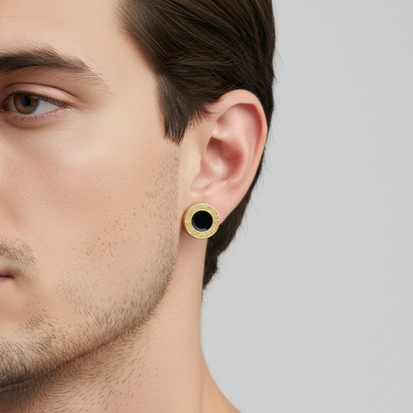 Close-up of a man wearing a gold earring with a black center on a neutral background