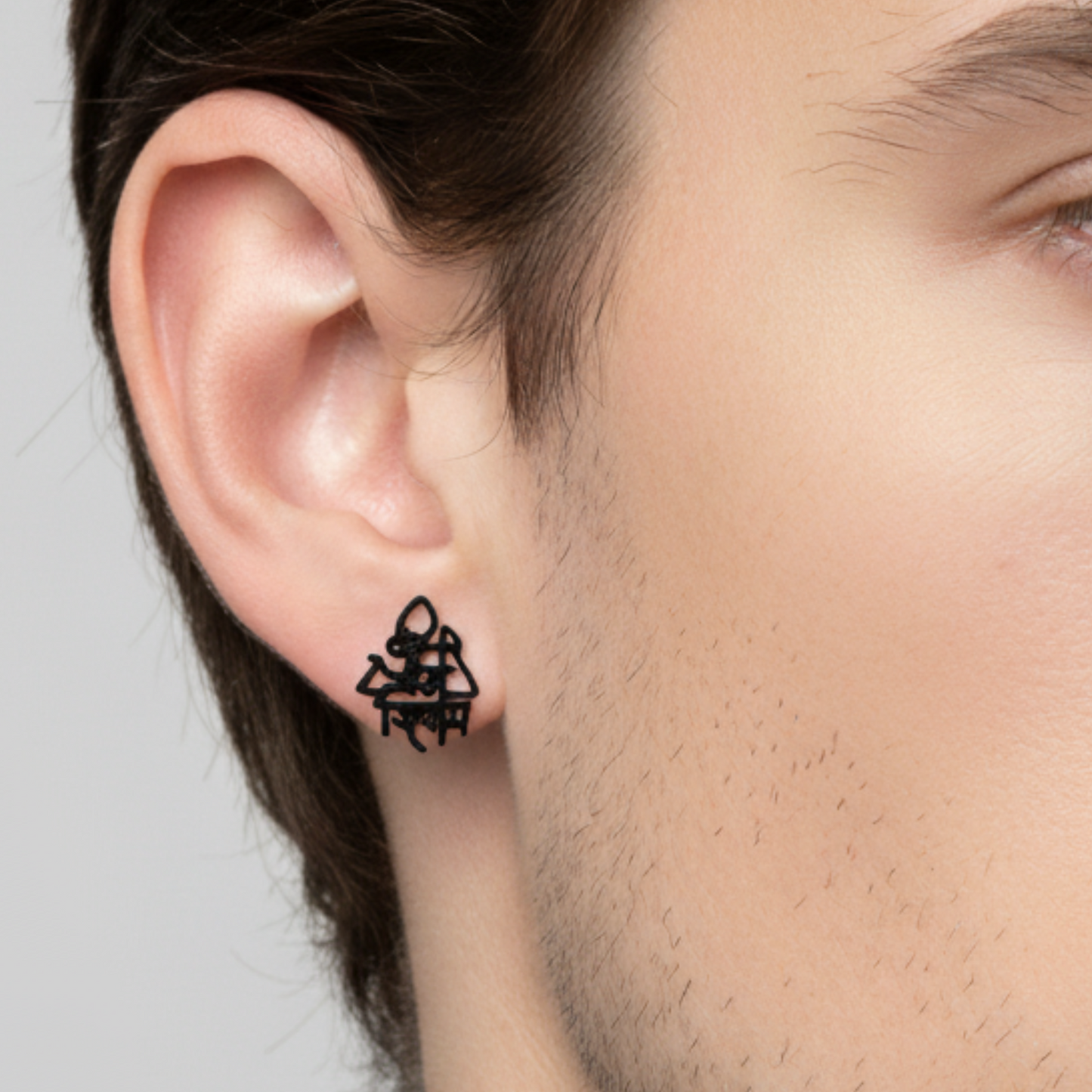 Close-up of an ear wearing a black geometric earring against a neutral background