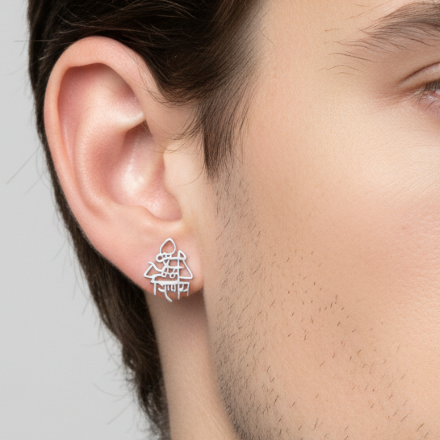 Silver geometric earring worn by a person on a neutral background
