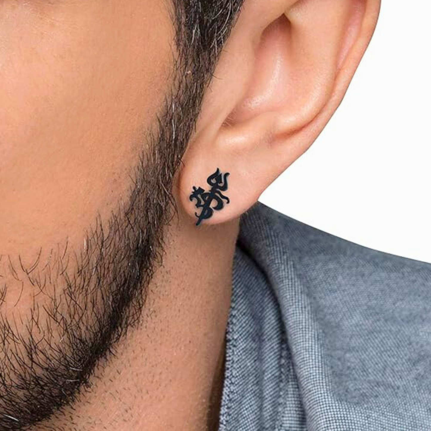 Black om trishul cross-shaped earring worn by a person with a neutral background