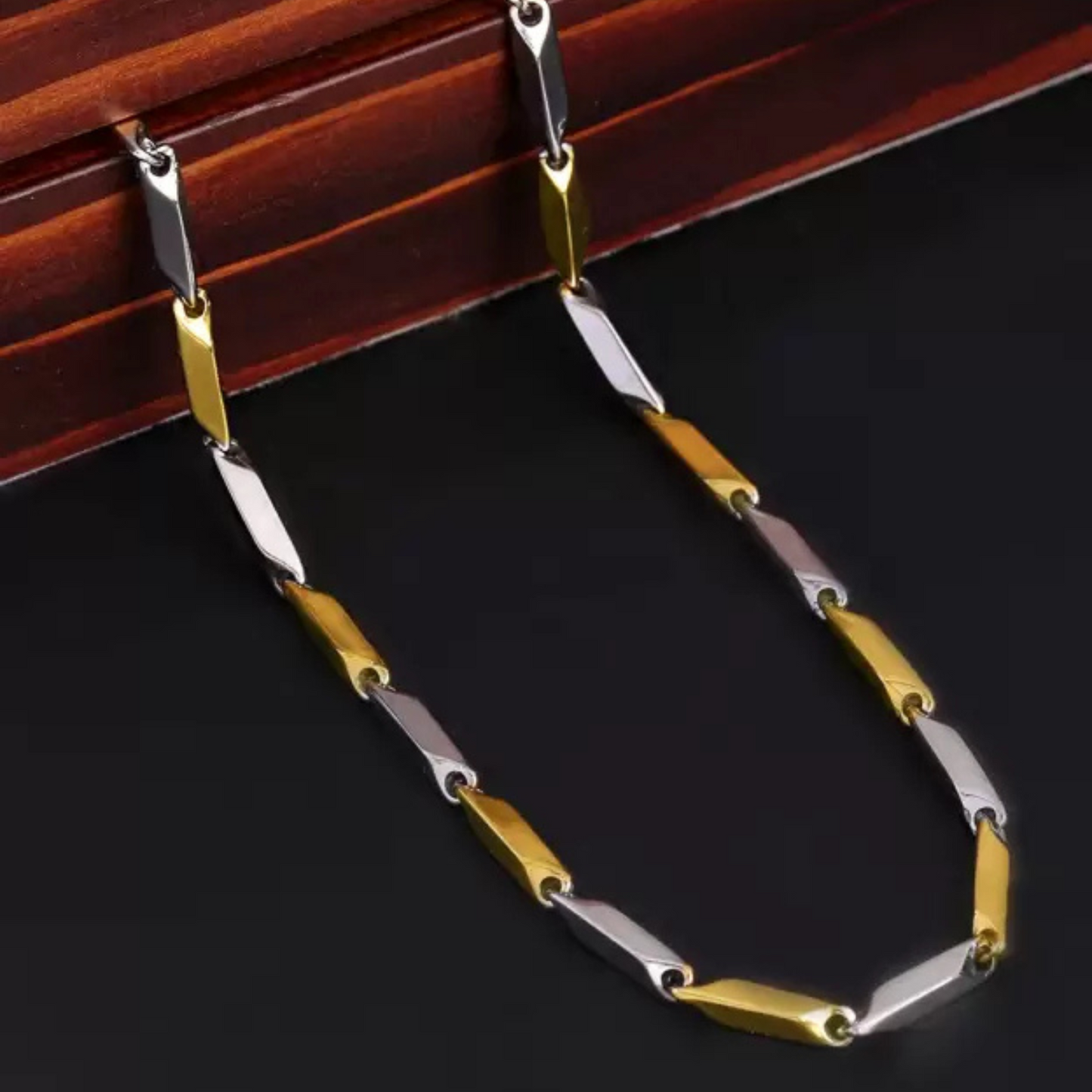 Gold and silver chain necklace on a dark surface with wooden background