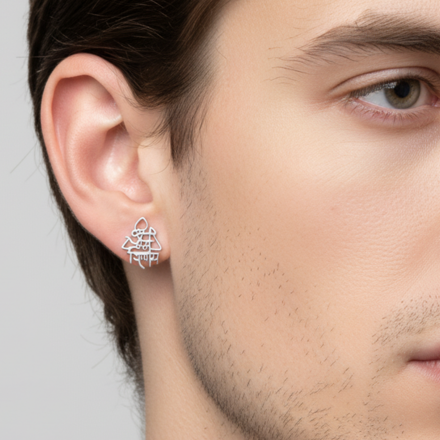 Close-up of a man wearing a silver triangular earring on a neutral background