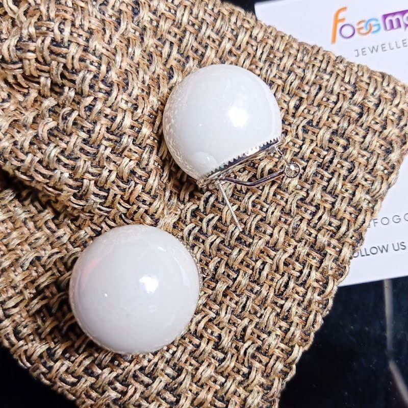 White spherical earrings on a textured fabric surface with a visible brand label.