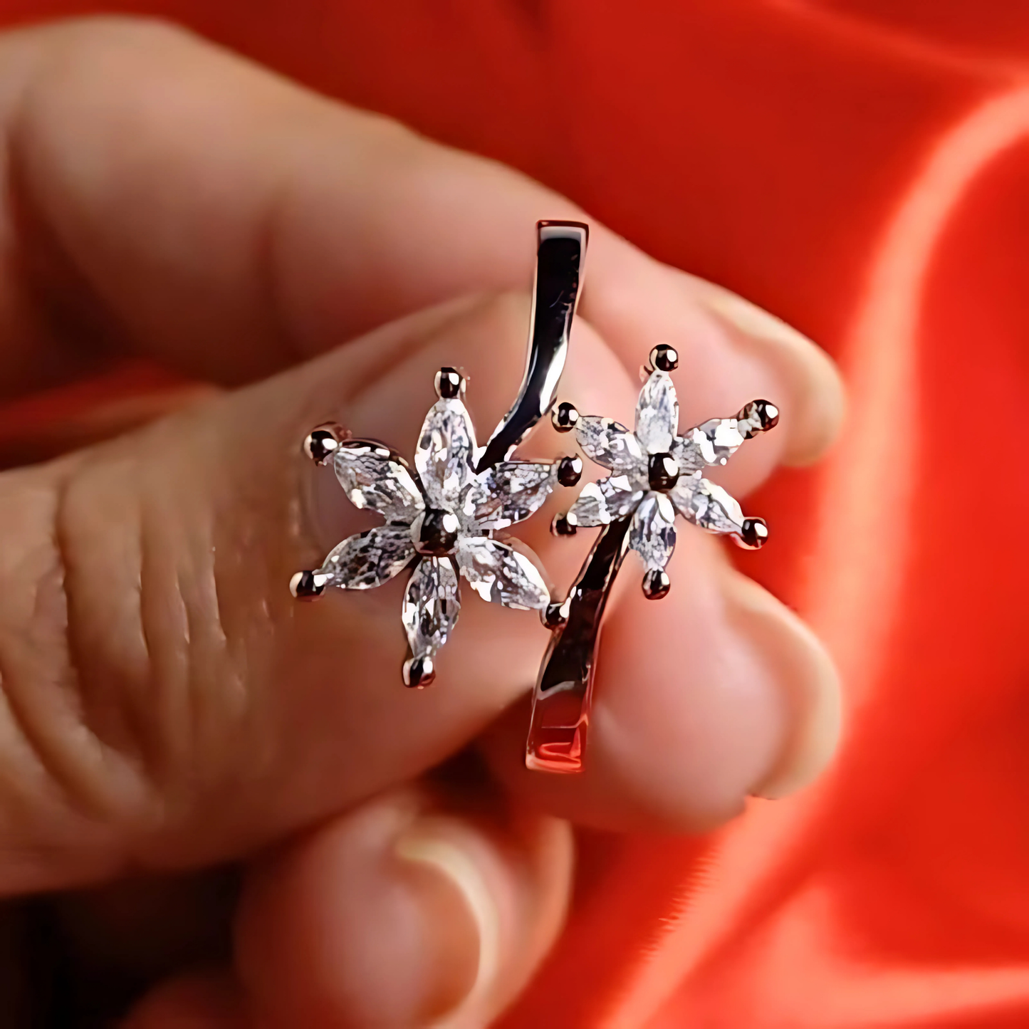 Silver floral pendant held between fingers against a red background