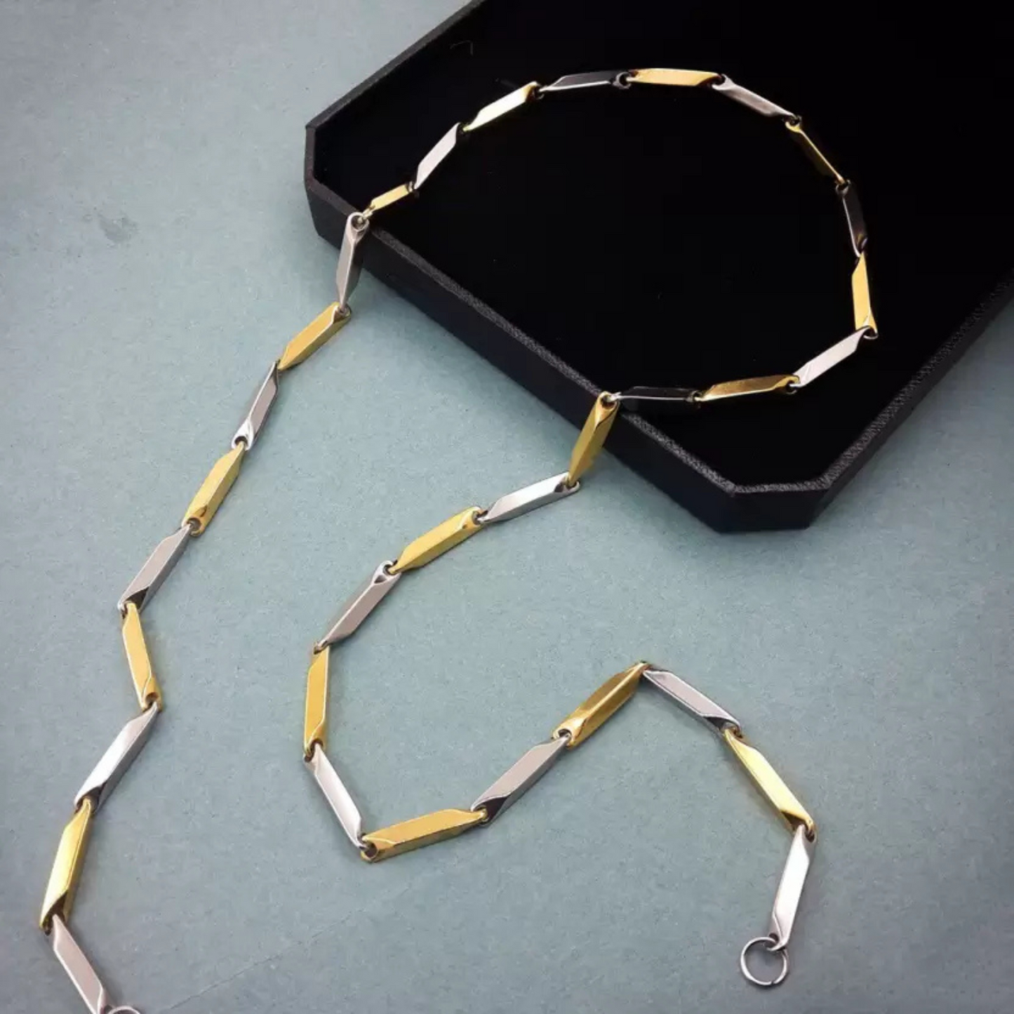 Gold and silver necklace on a green surface with a black box in the background
