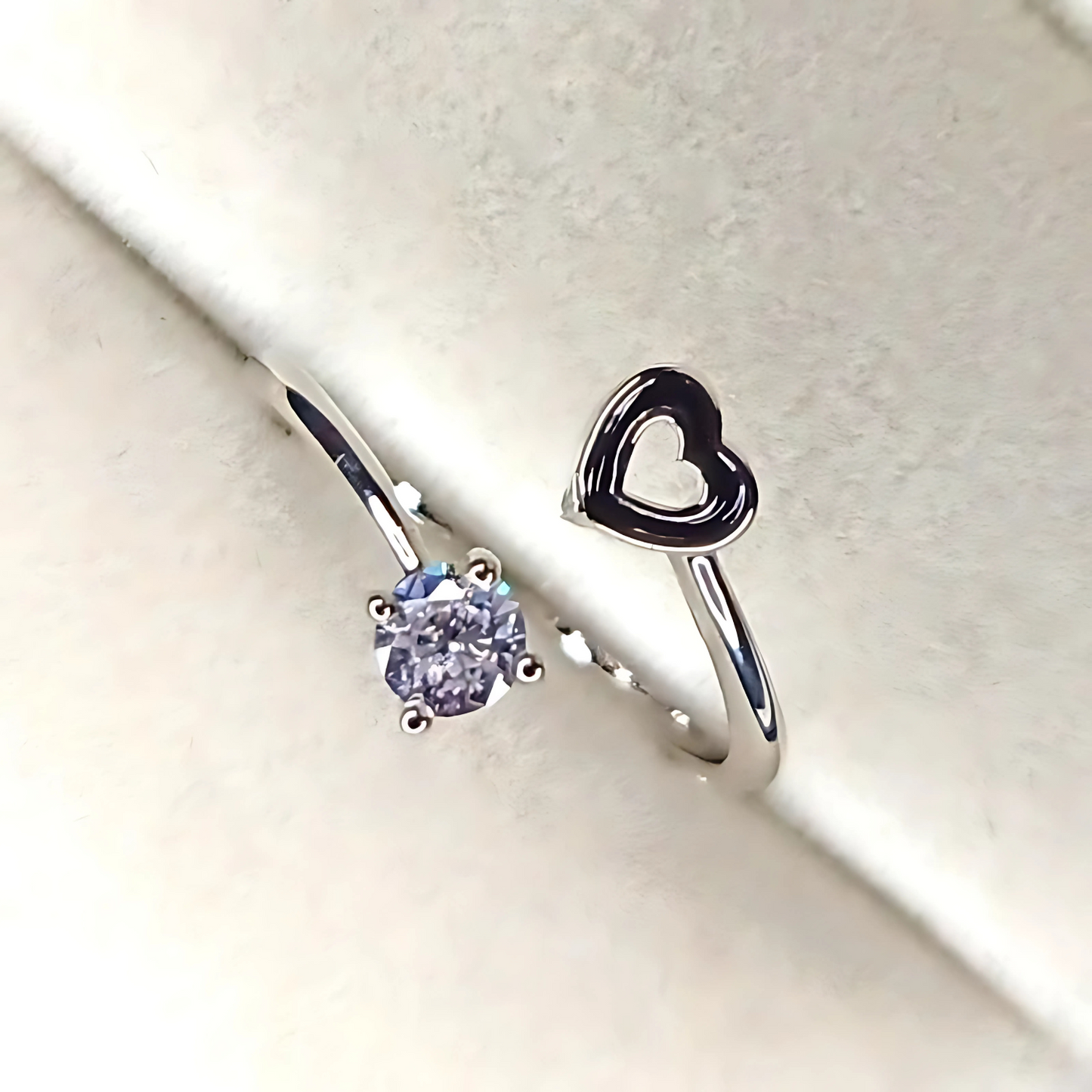 Two rings on a light gray background, one with a heart-shaped design and the other with a gemstone.