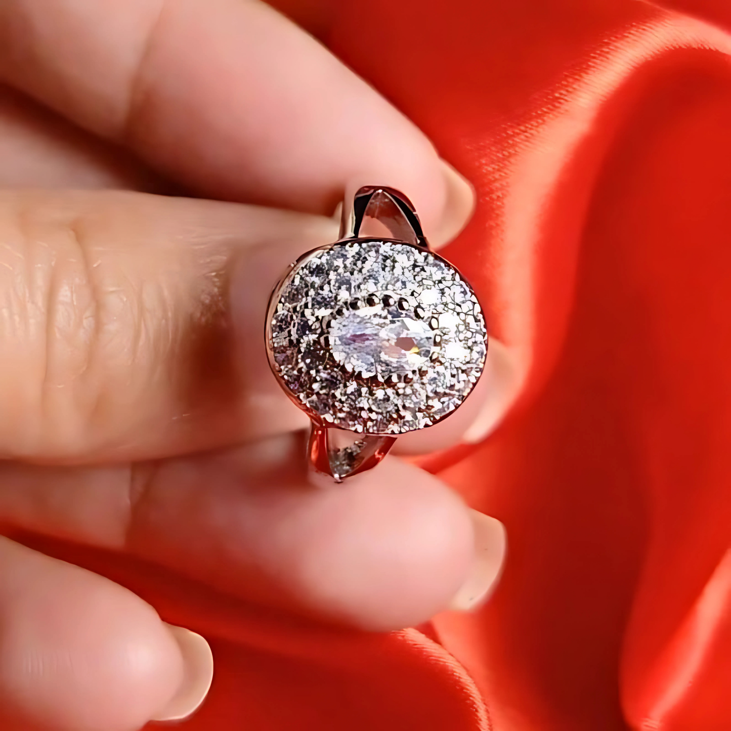 Close-up of a hand holding a diamond ring against a red fabric background