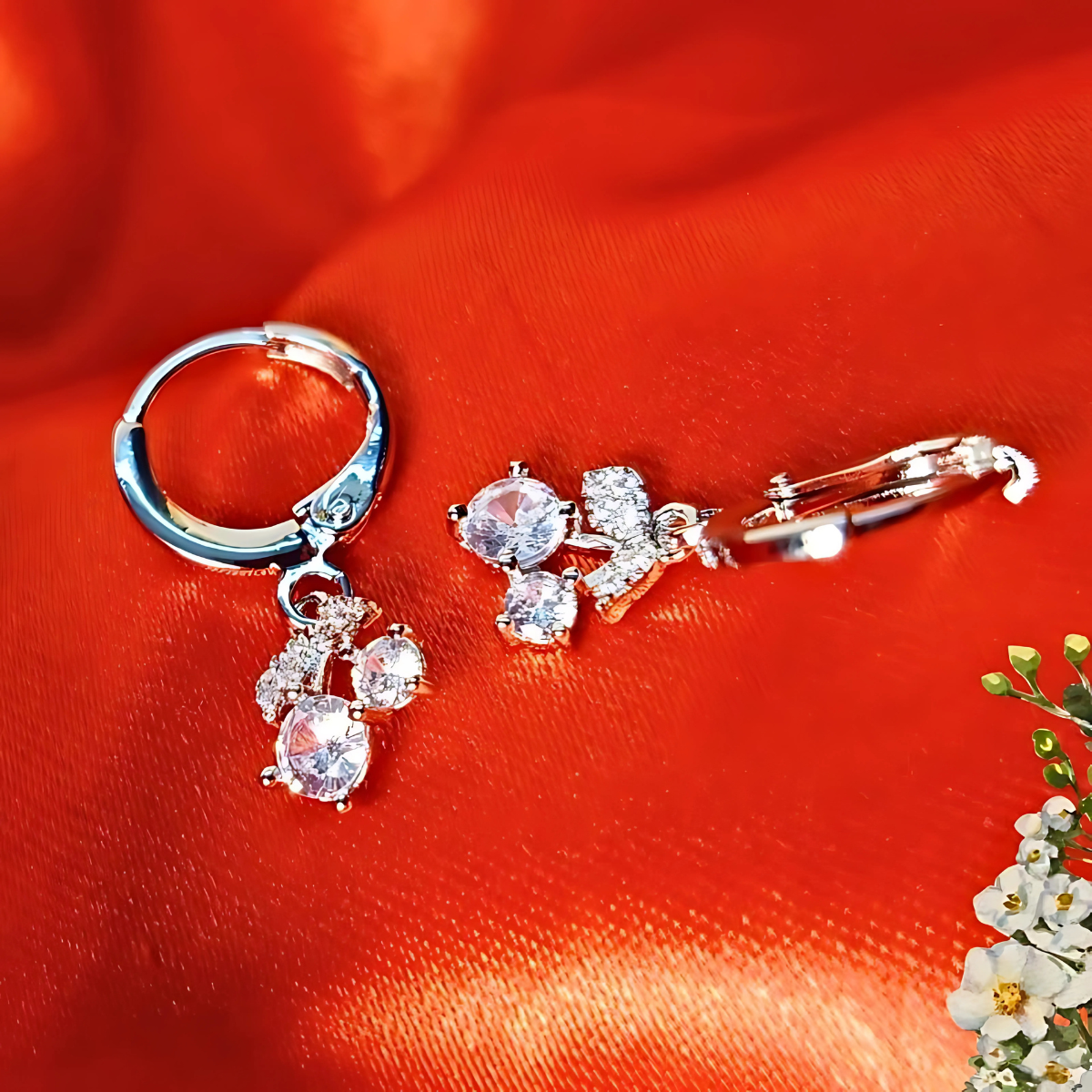 Silver earrings with clear stones on a red fabric background