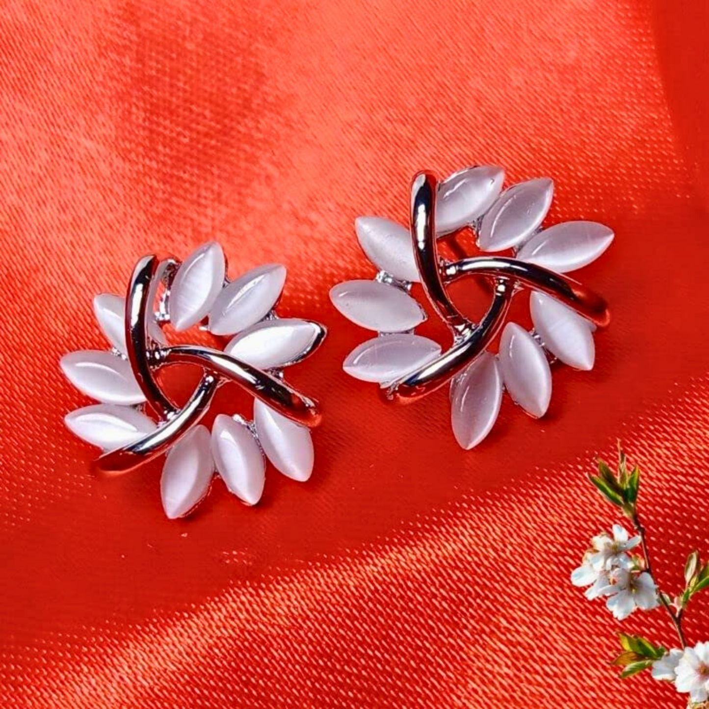 Pair of floral earrings with white petals and silver loops on a red background