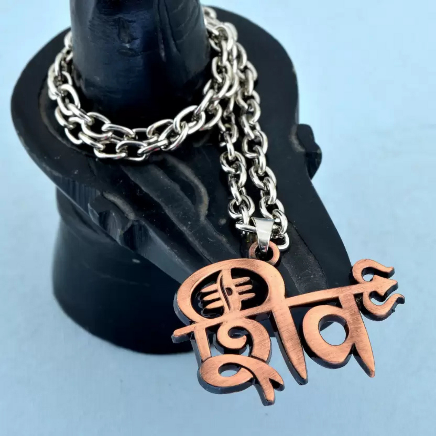 Necklace with a copper pendant on a black stand against a light blue background
