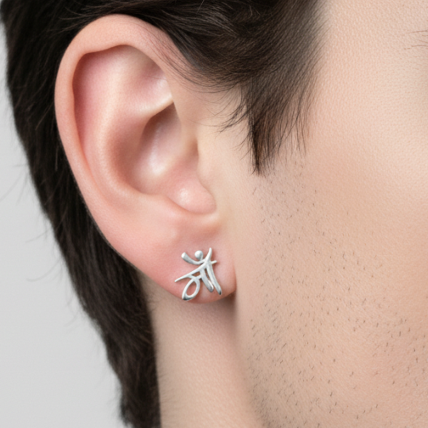 Silver earring worn on an ear with a neutral background