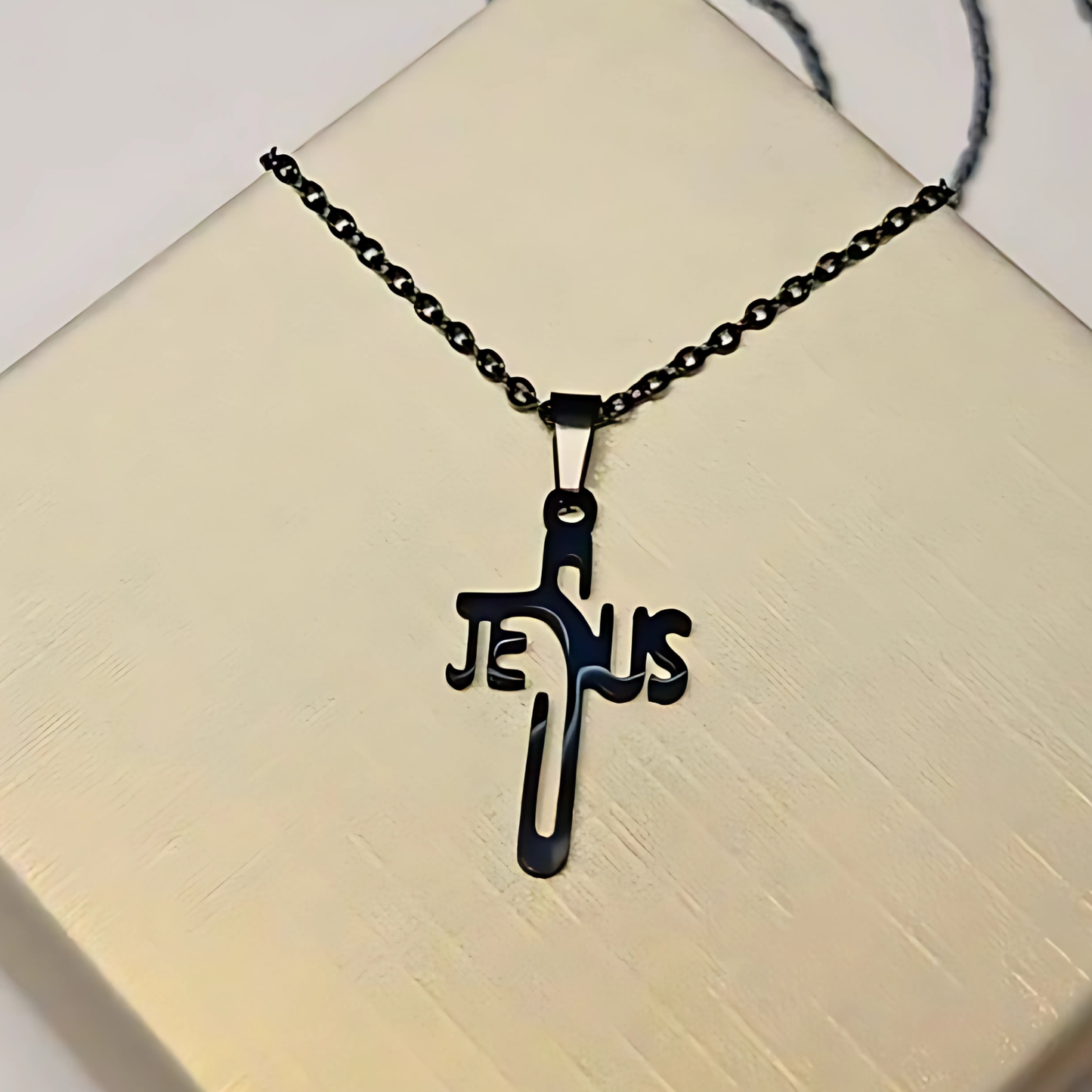 Black 'Jesus' cross necklace on a beige surface