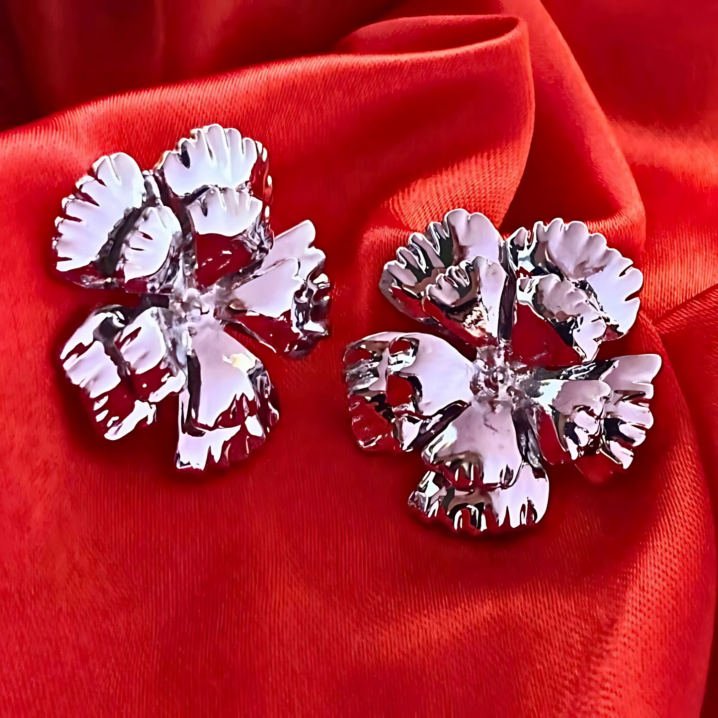 Silver flower-shaped earrings on a red fabric background