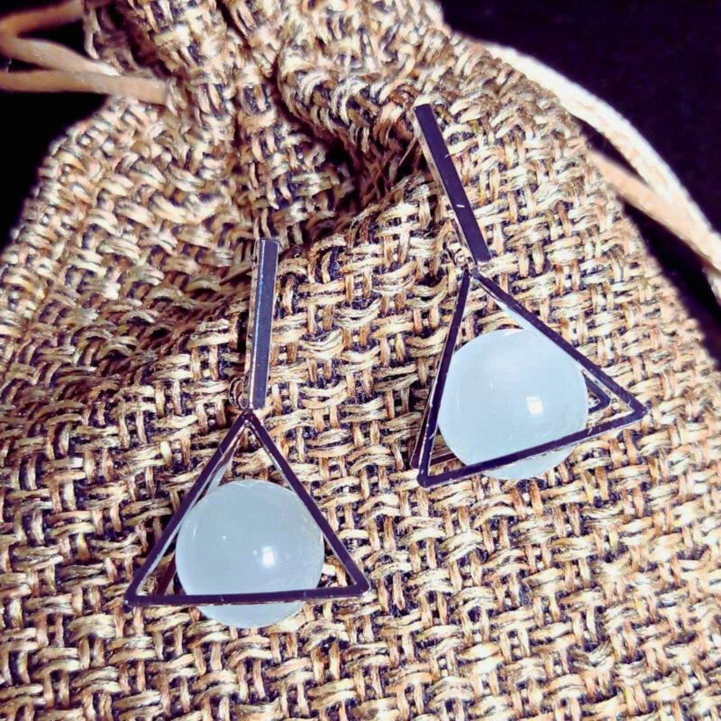 Triangle-shaped earrings with light blue stones on a textured fabric background