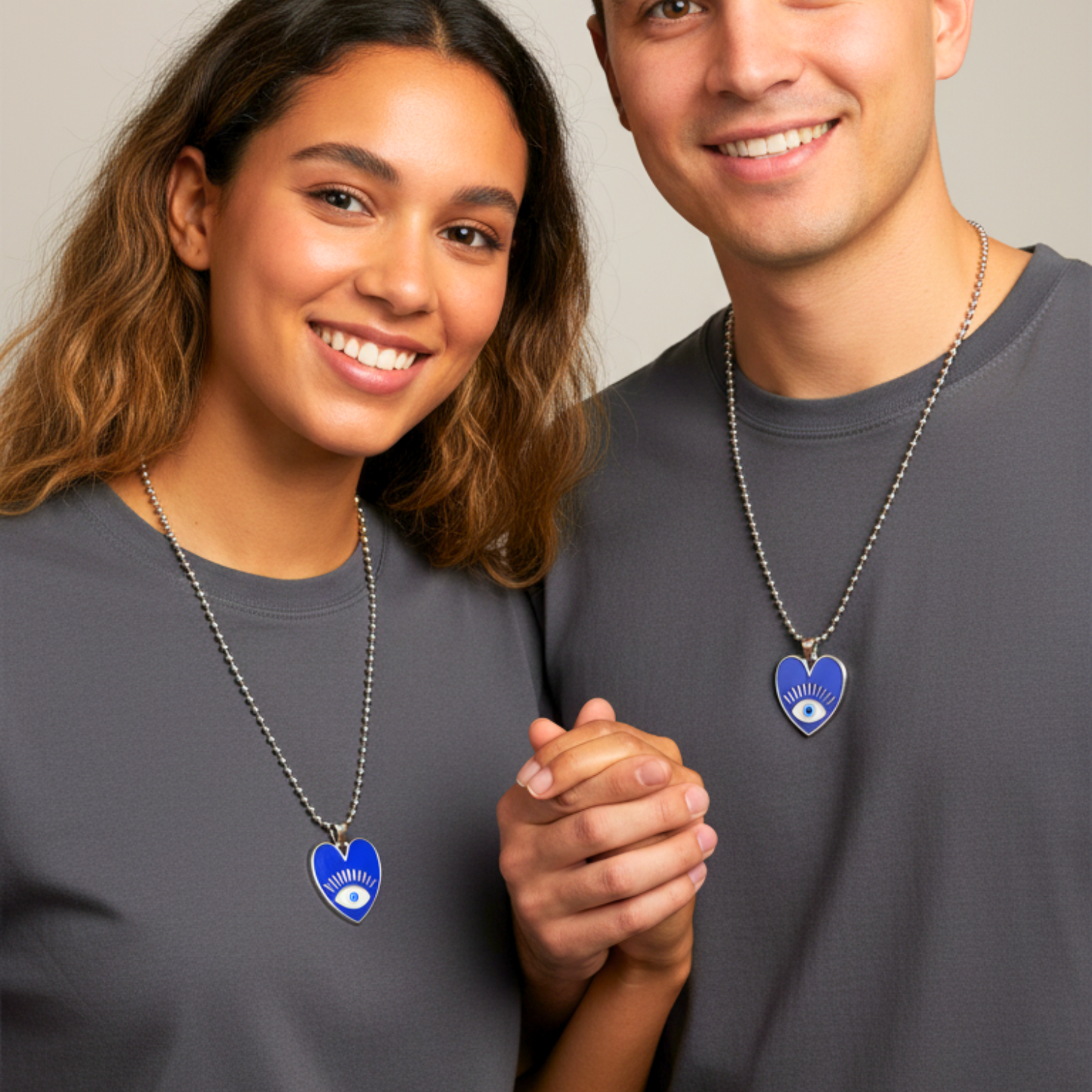 Two people wearing matching blue heart-shaped necklaces with eye designs on a plain background